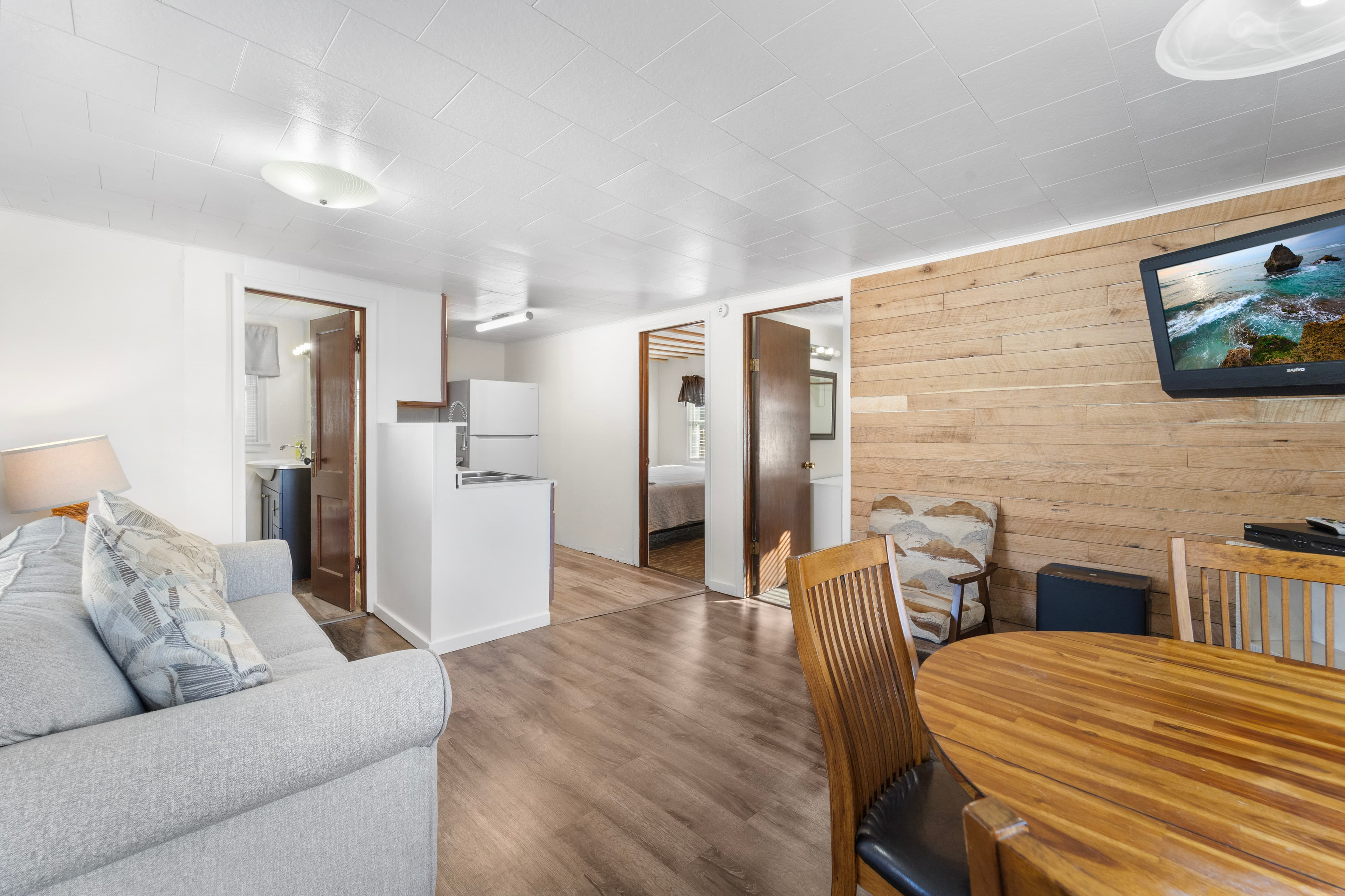 A cozy living space featuring a sofa, dining table, and kitchenette with wooden accents.