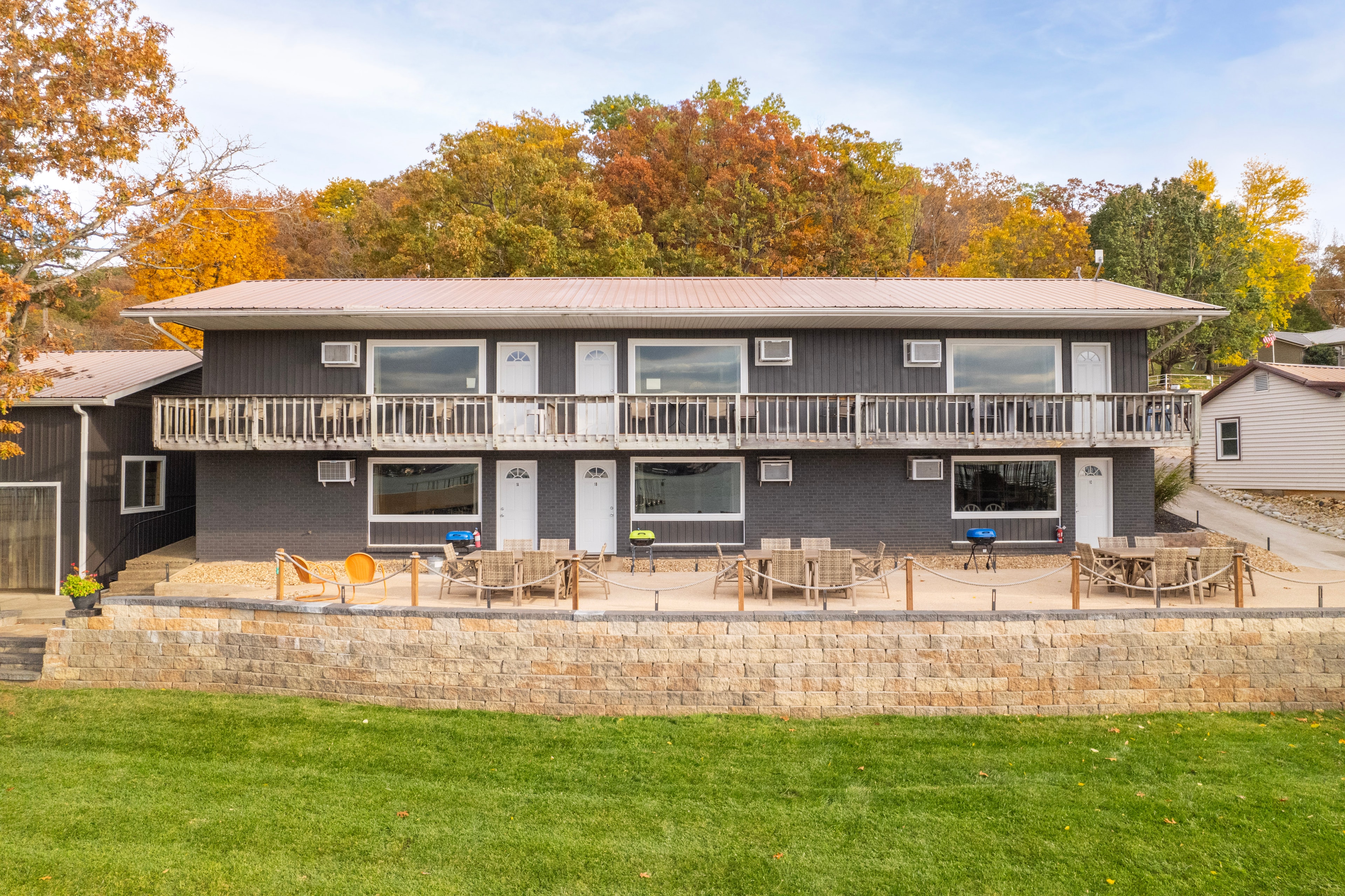 Two-story modern building with a patio overlooking a grassy area and vibrant autumn trees.