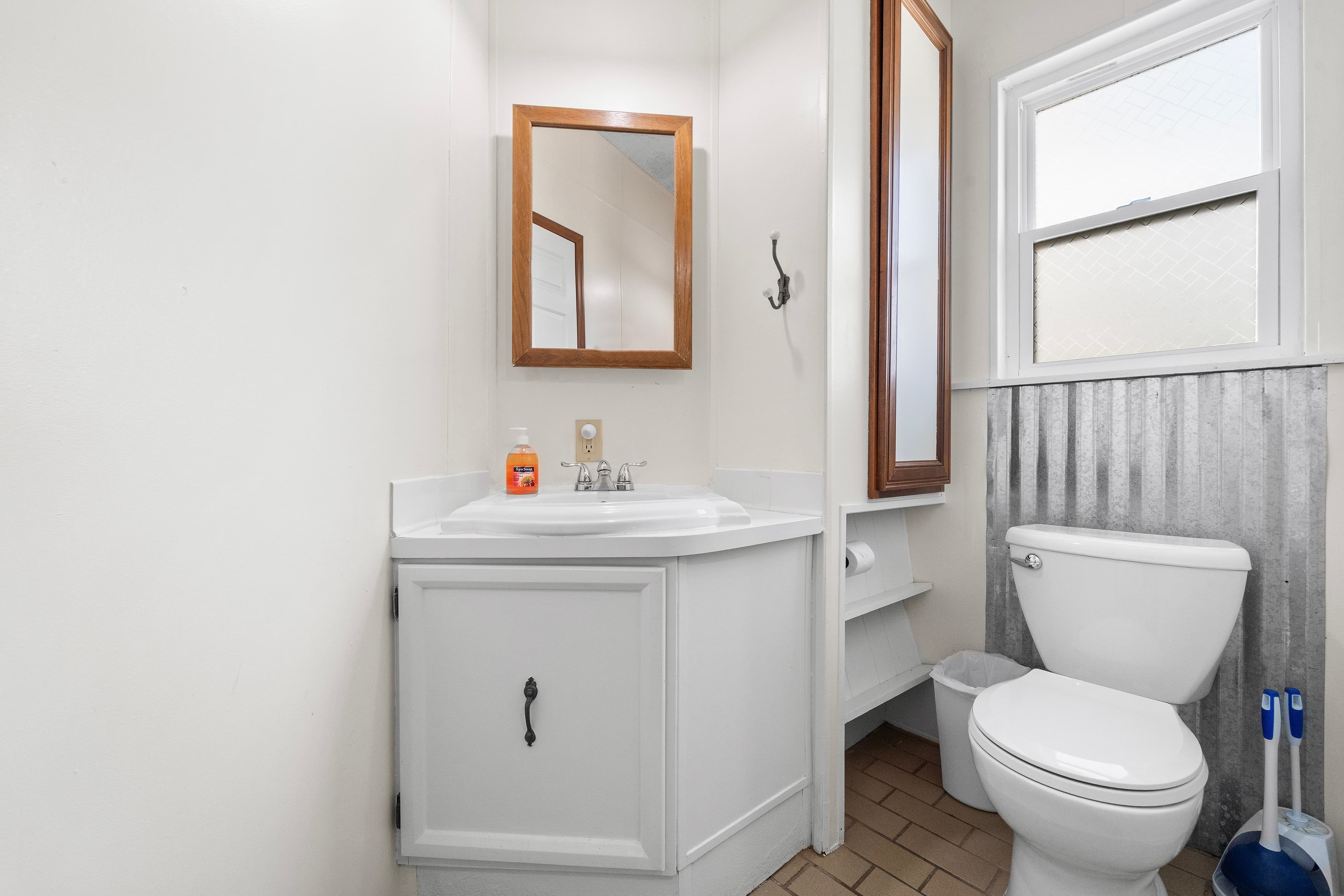 A compact bathroom featuring a white sink, mirror, and toilet, with a window and tiled floor.