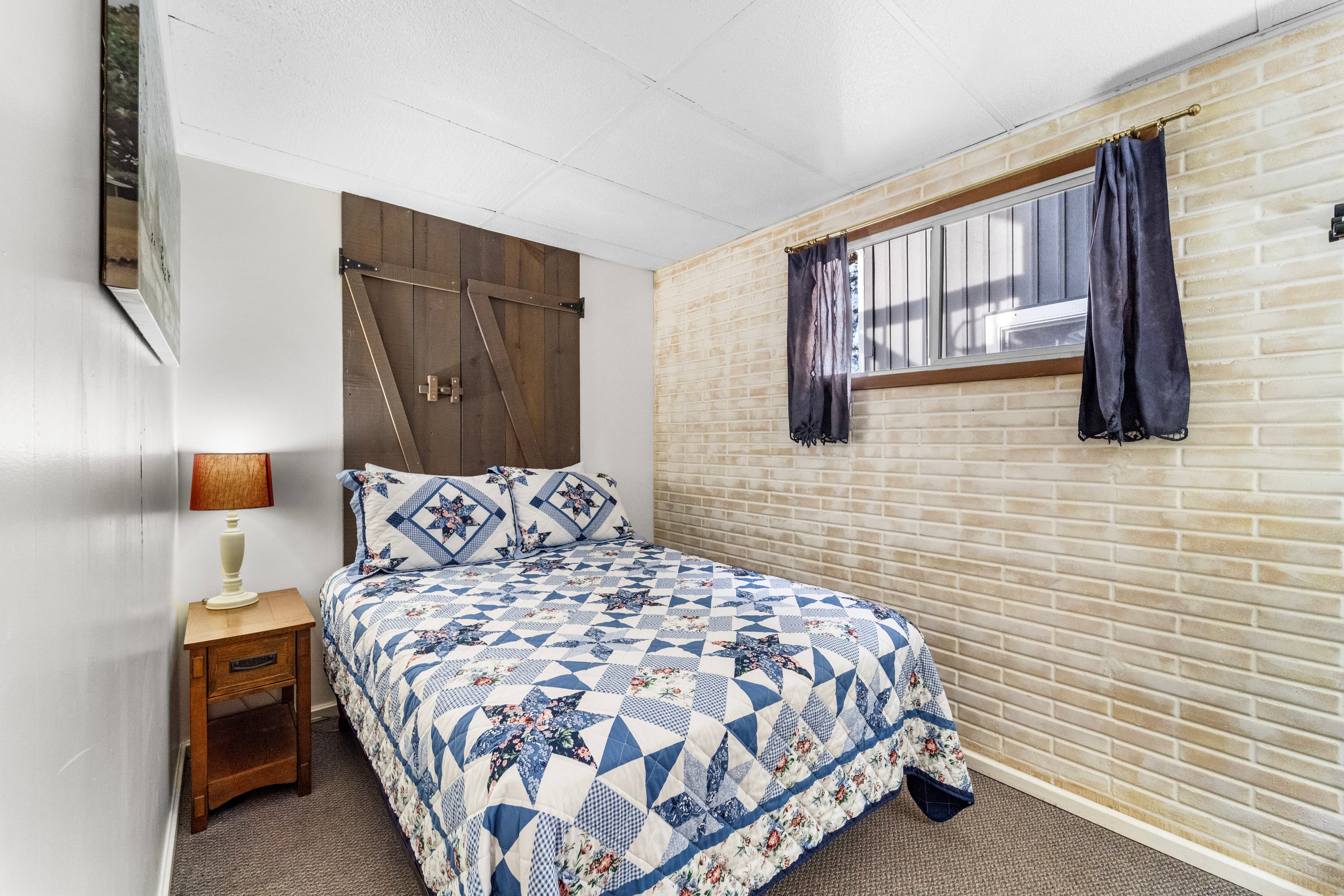 A cozy bedroom featuring a quilted bedspread, wooden barn doors, and a small bedside table with a lamp.