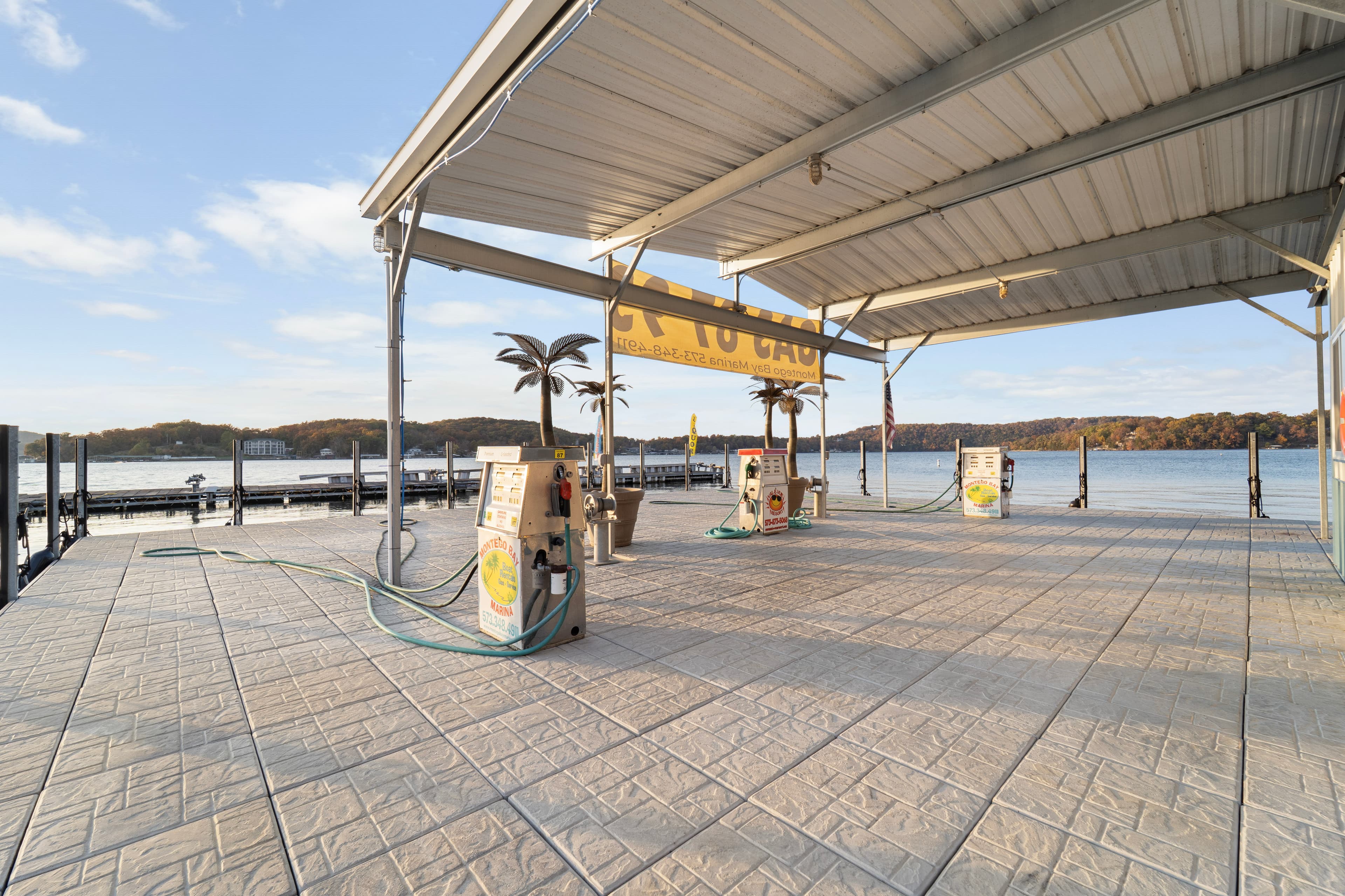 A weathered boat dock with fuel pumps overlooks a tranquil lake under a clear sky.