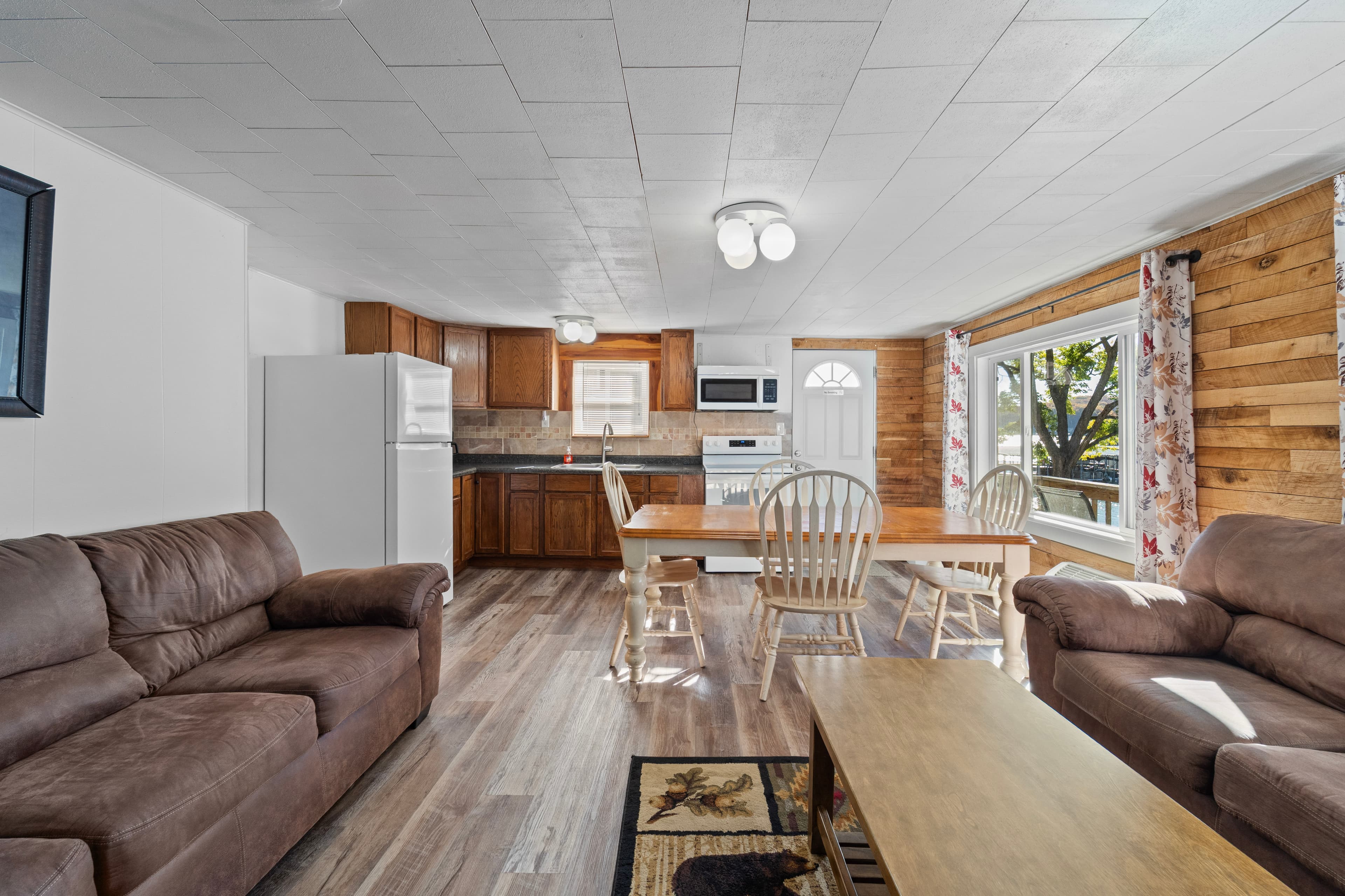 A cozy, well-lit kitchen and living area featuring brown sofas, a dining table, and modern appliances.