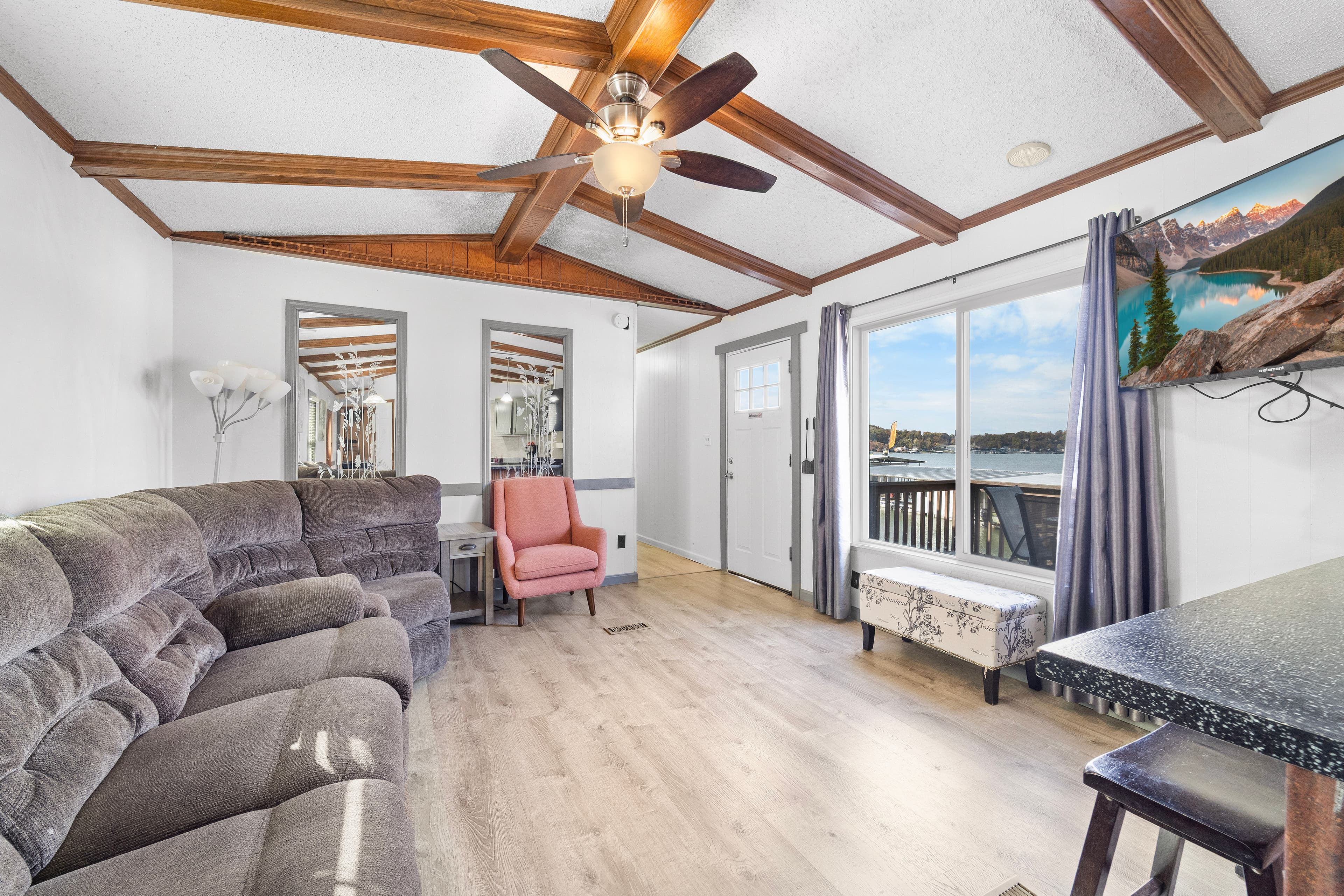 A cozy living room with a ceiling fan, plush seating, and large windows showcasing a scenic view.