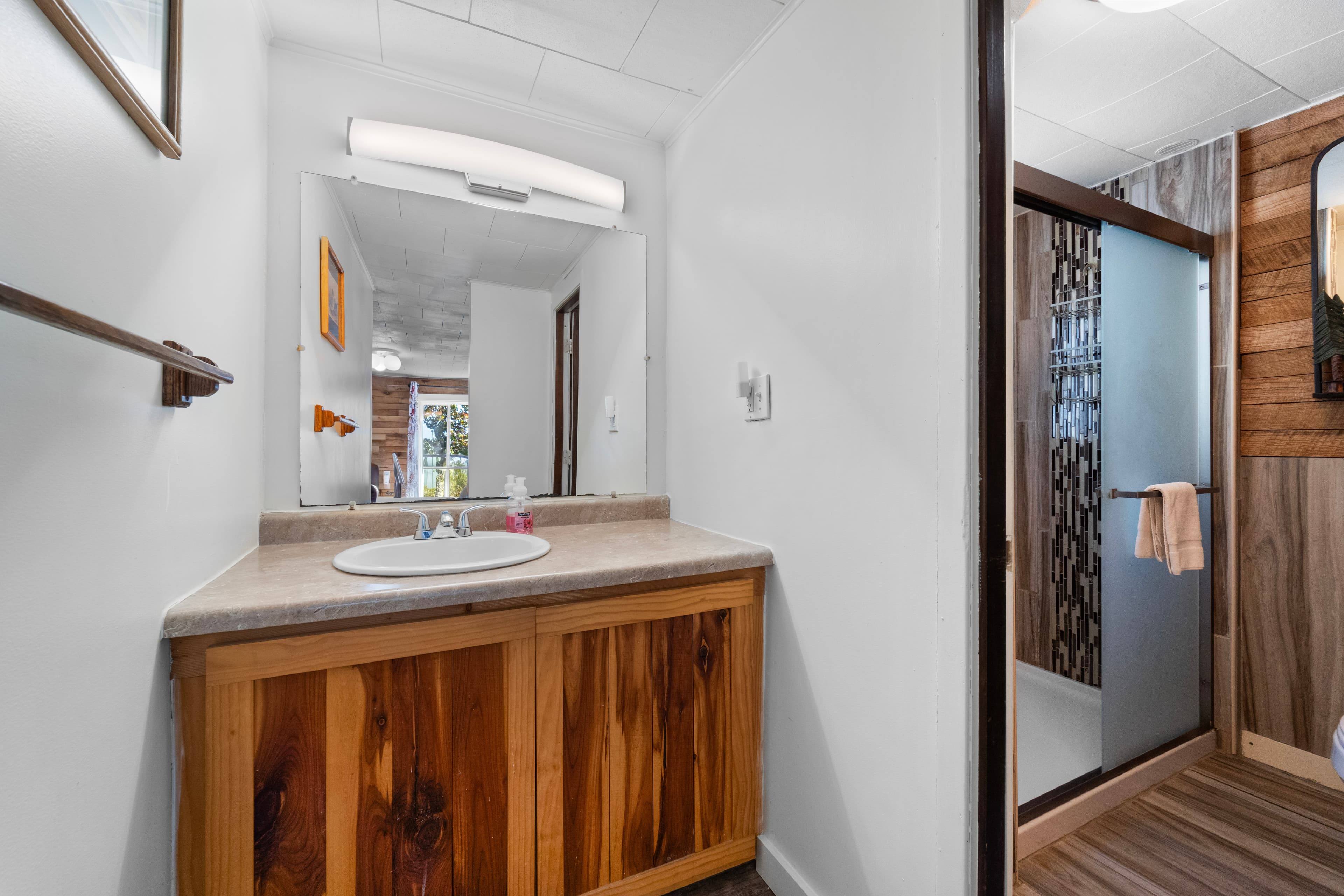 A well-lit bathroom featuring a wood vanity, mirror, and a glass shower enclosure.