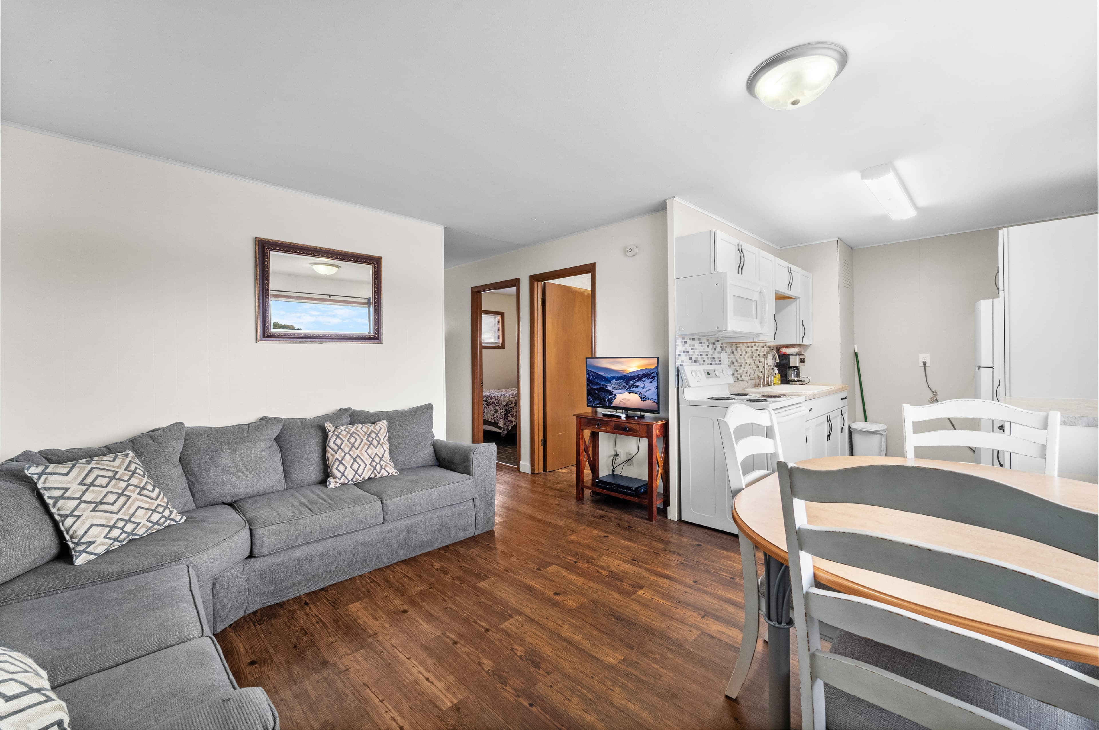 A cozy living area featuring a gray sofa, dining table, and a kitchen in the background.