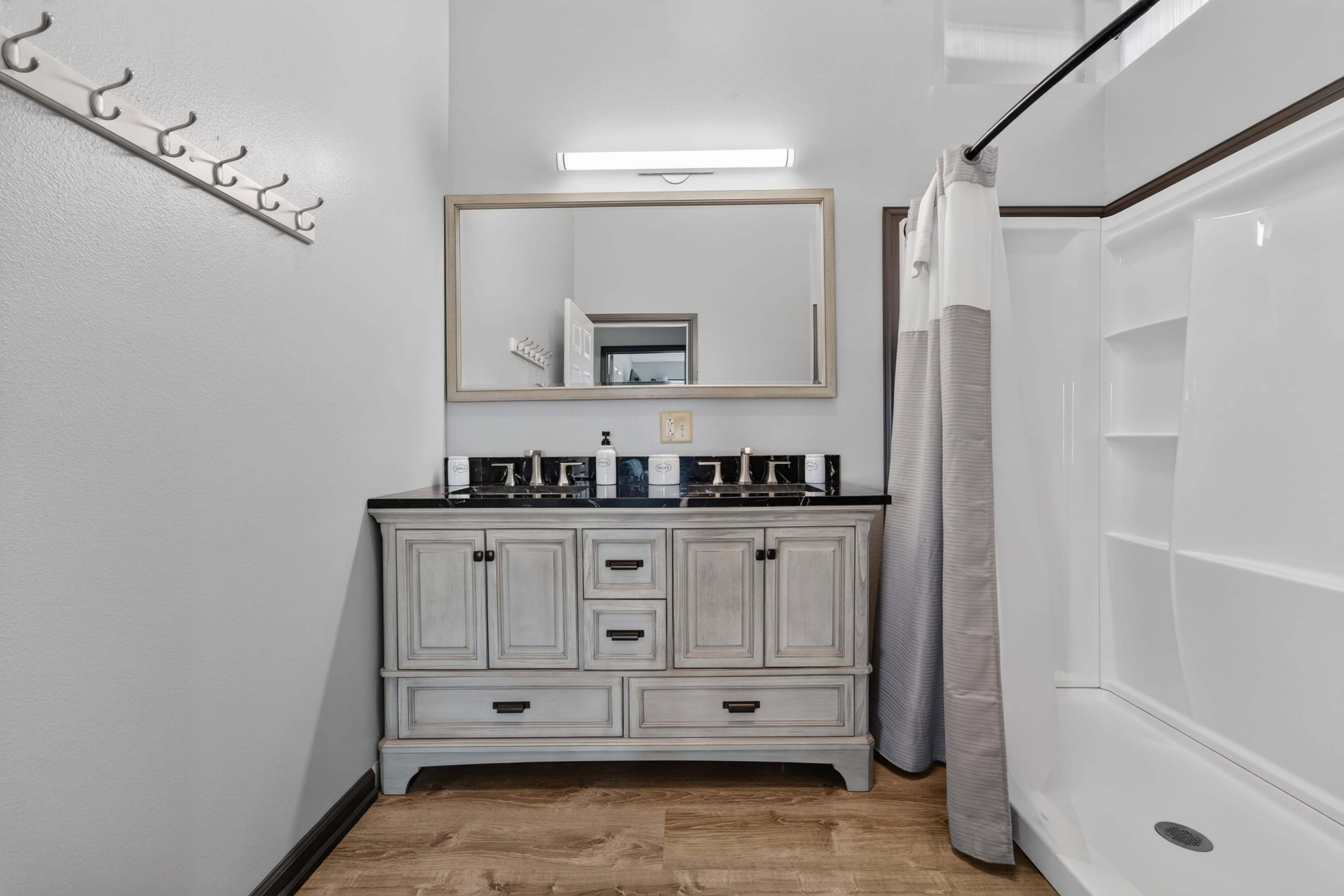 A modern bathroom featuring a wooden vanity with a large mirror, a shower, and several wall hooks.