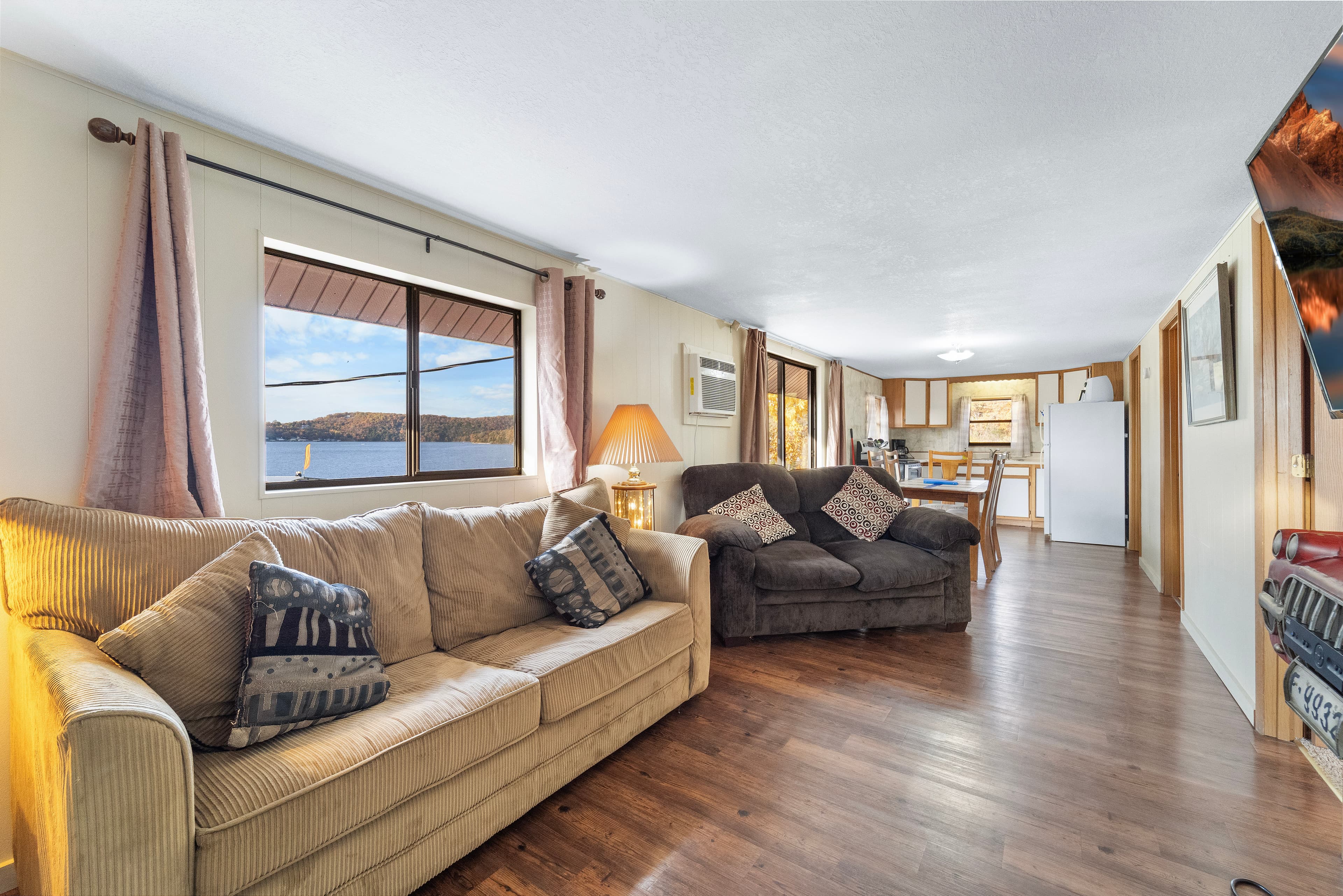 Cozy living room with a lake view, featuring a beige couch, dark sofa, and dining area.