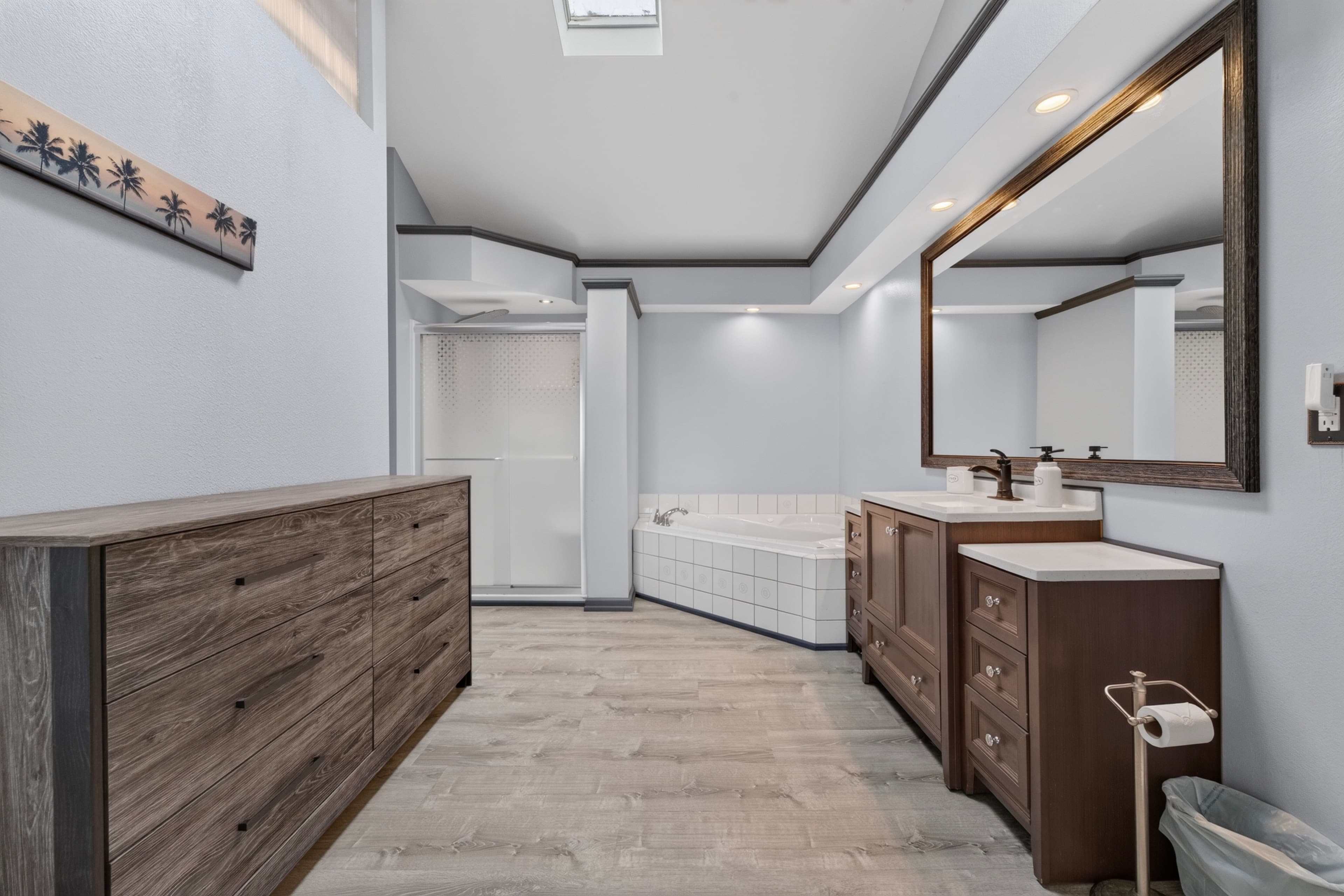 A spacious, modern bathroom featuring a large bathtub, double vanity, and natural light from a skylight.