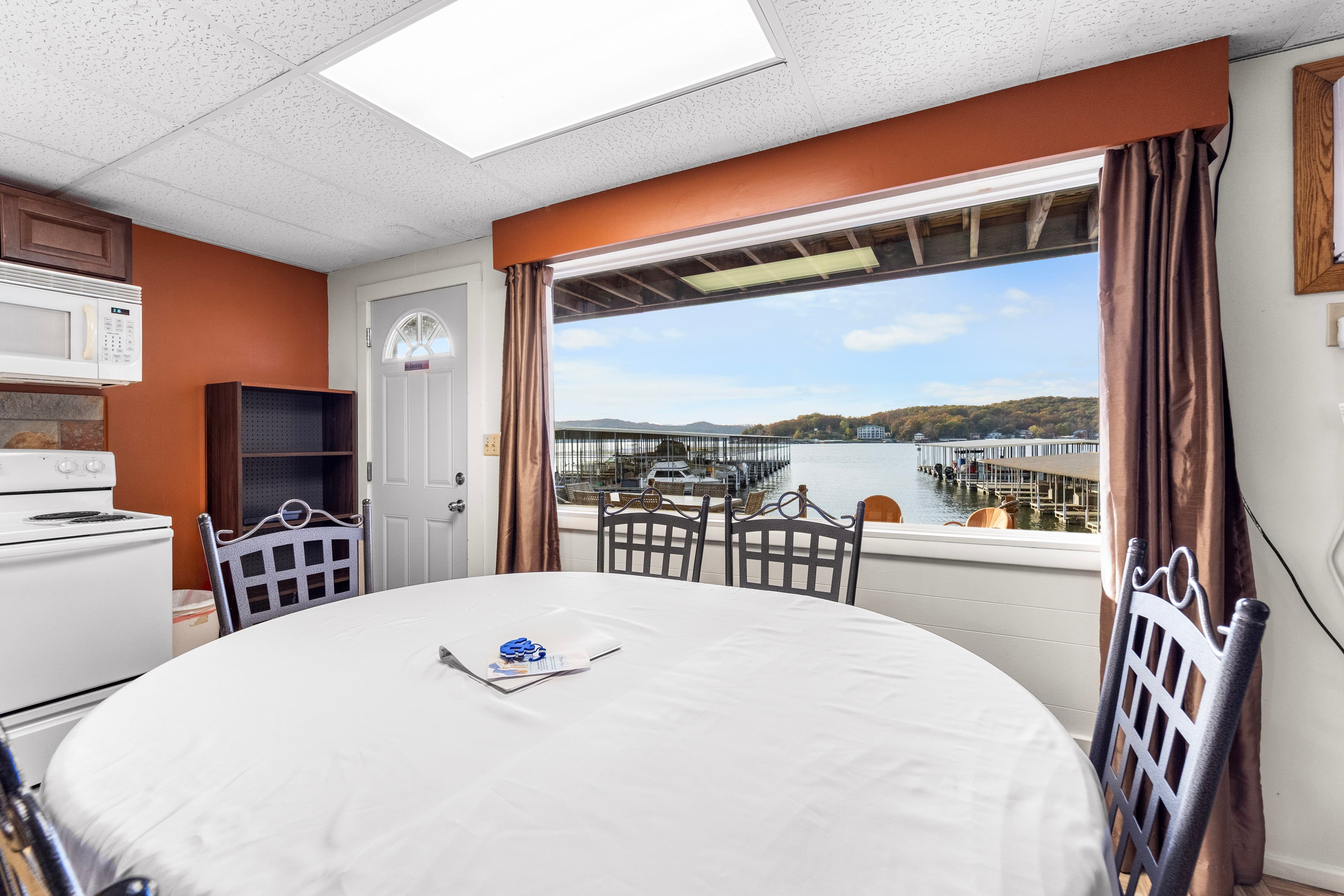 A cozy kitchen with a round table and a view of a lake and dock through a large window.