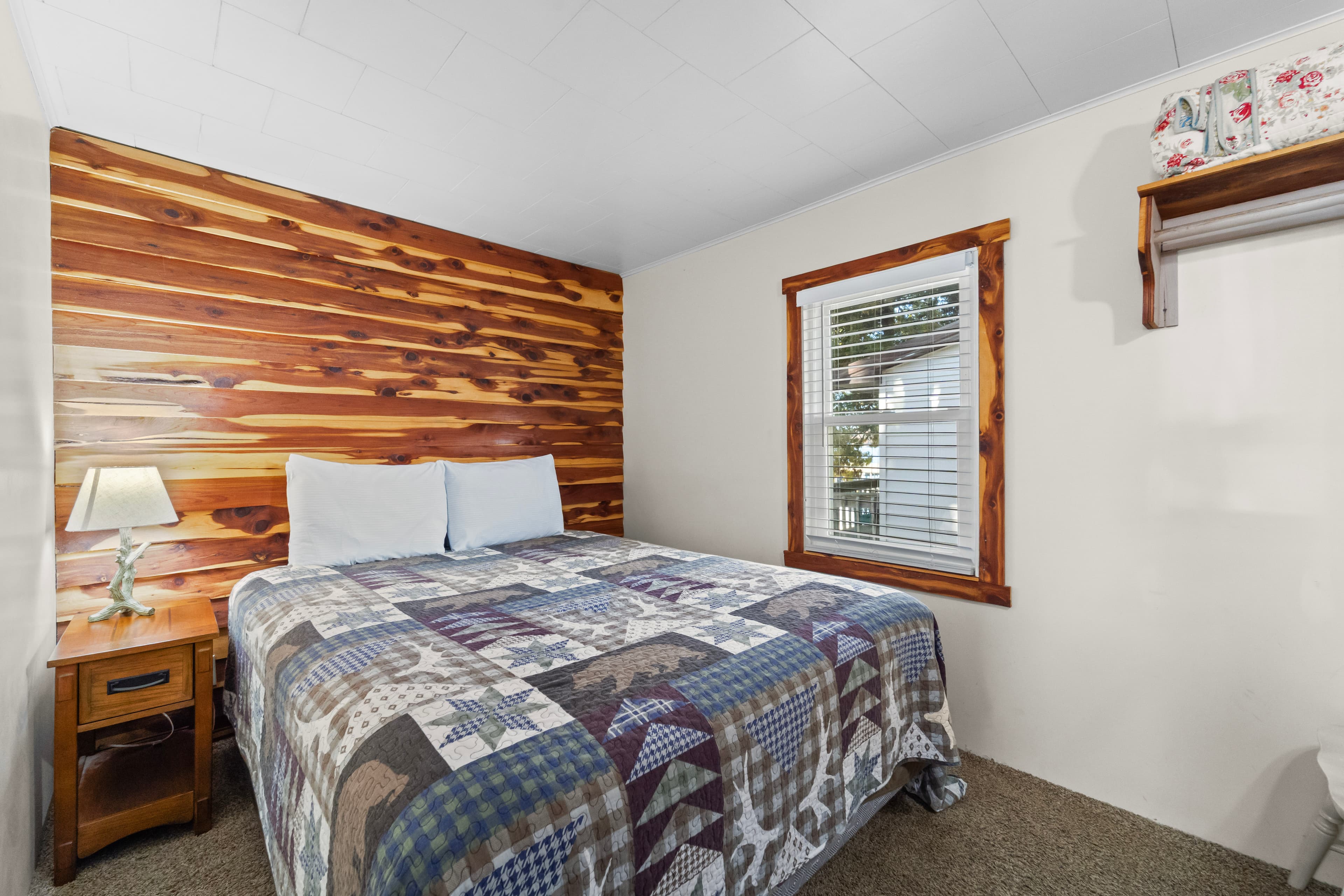 Cozy bedroom featuring a bed with a patterned quilt and a wooden accent wall.