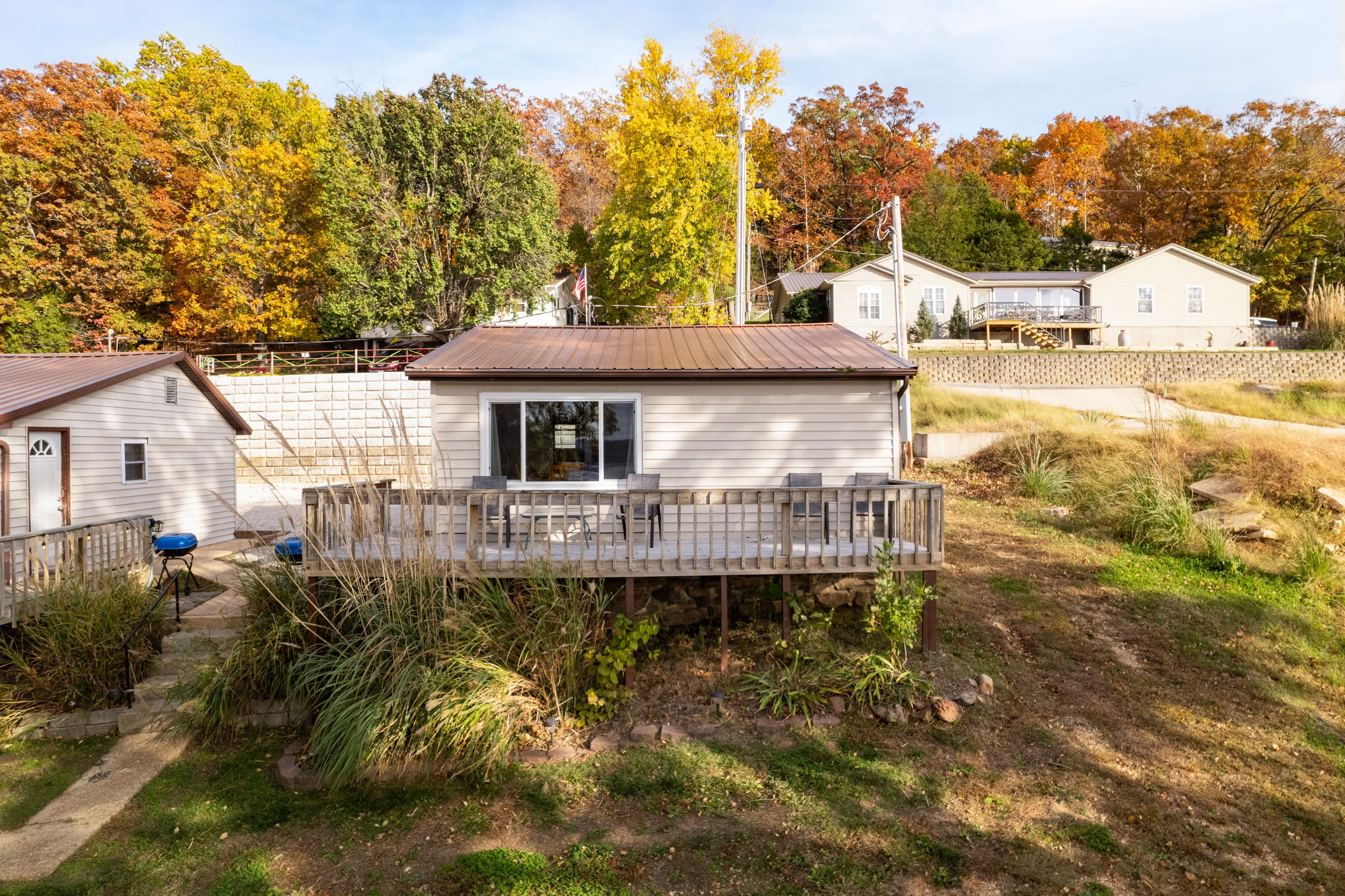 A small house with a deck surrounded by colorful autumn trees and neighboring homes.