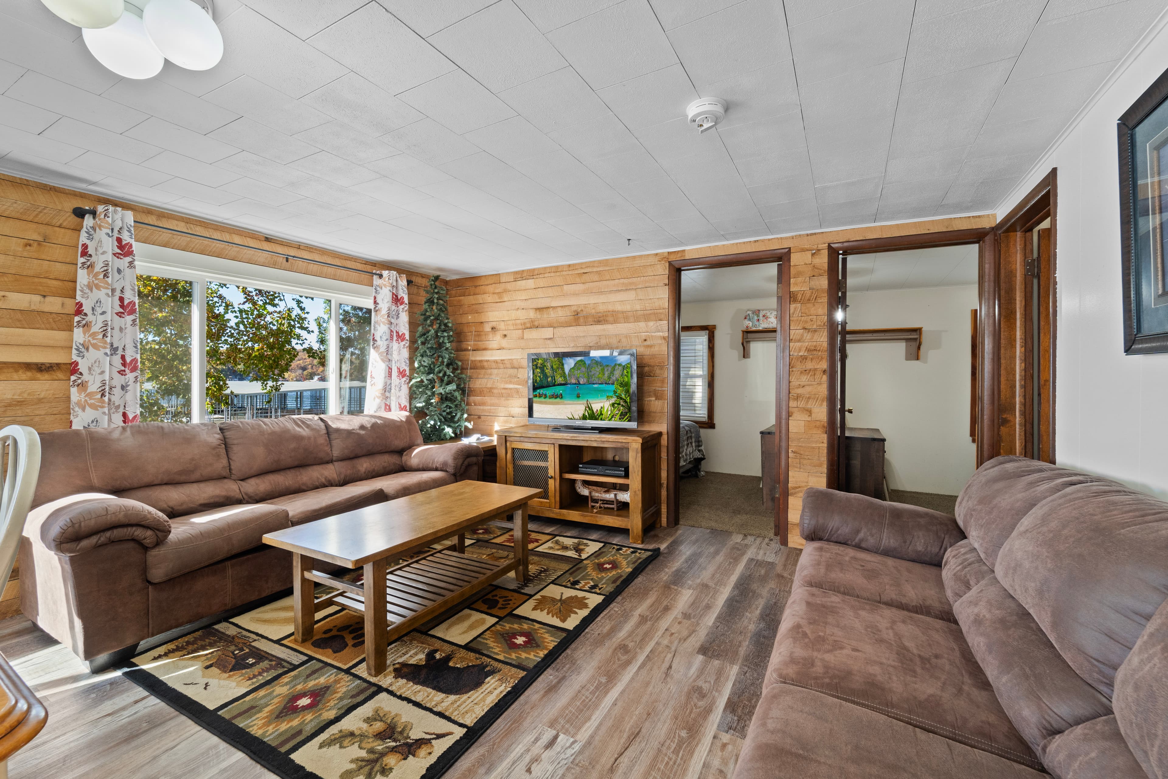 Cozy living room featuring two sofas, a wooden coffee table, a TV, and large windows with natural light.