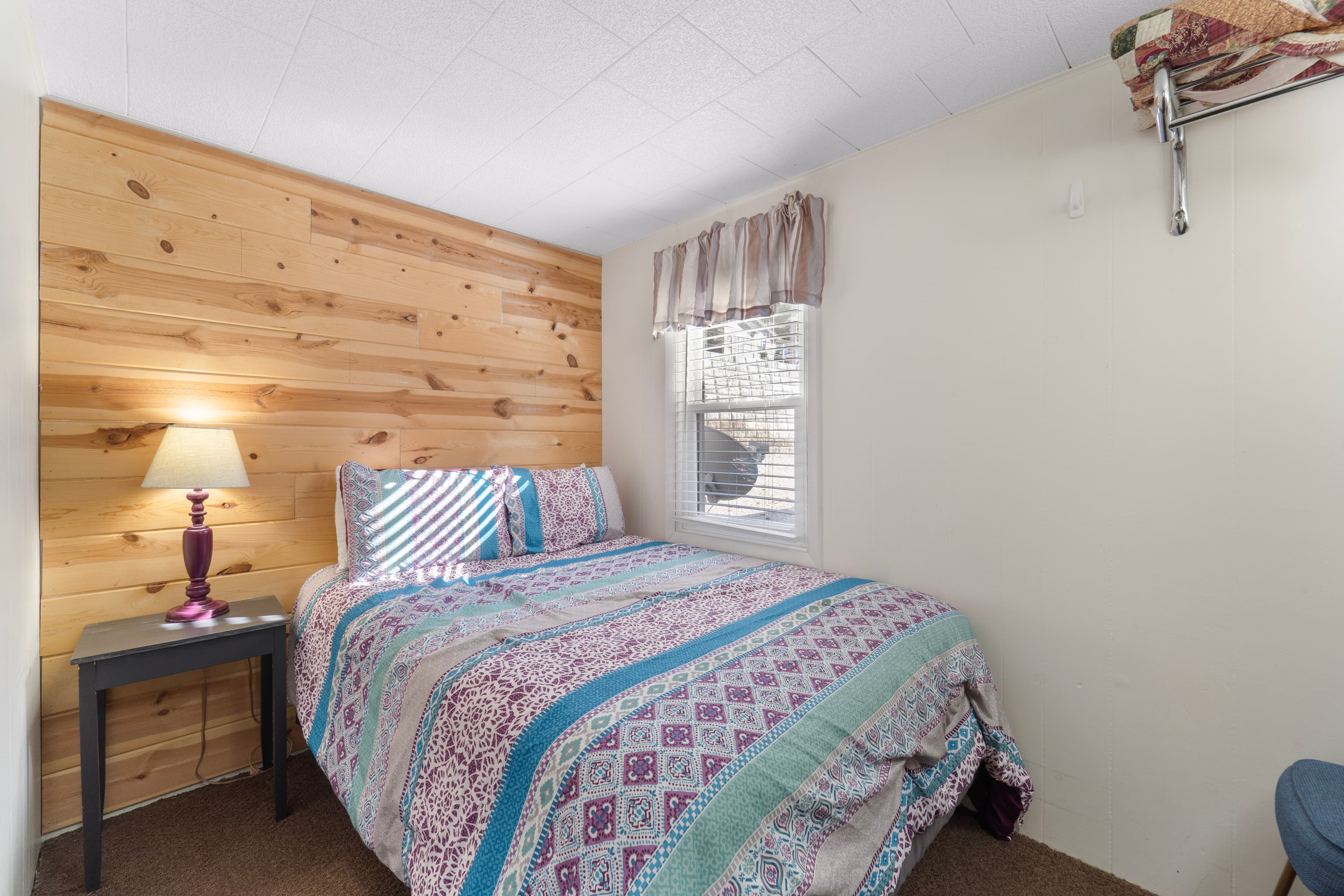 Cozy bedroom with a queen-sized bed, wooden accent wall, and a lamp on a side table.