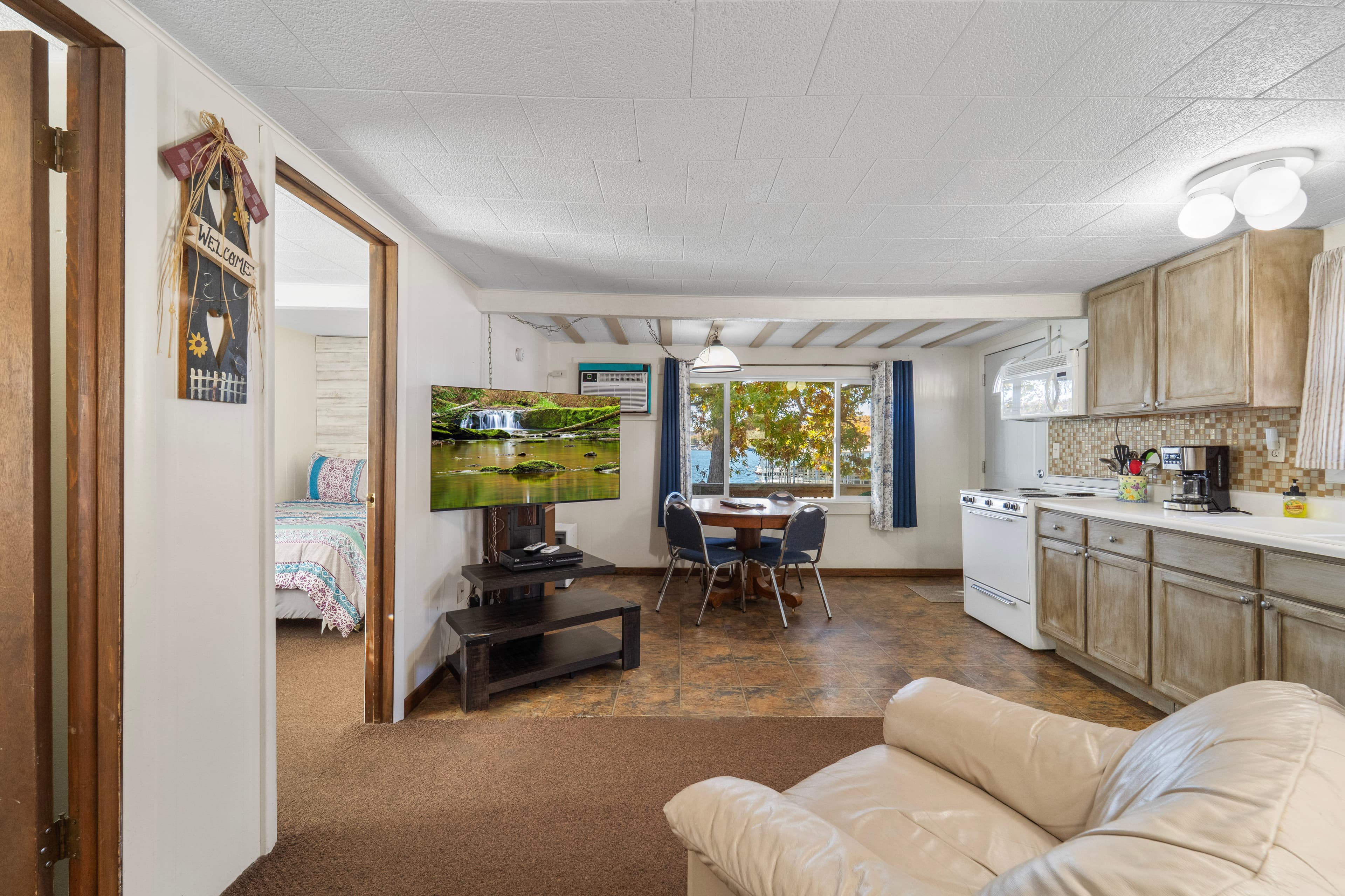 Cozy open living space featuring a kitchen, dining area, and a view of the outdoors through large windows.