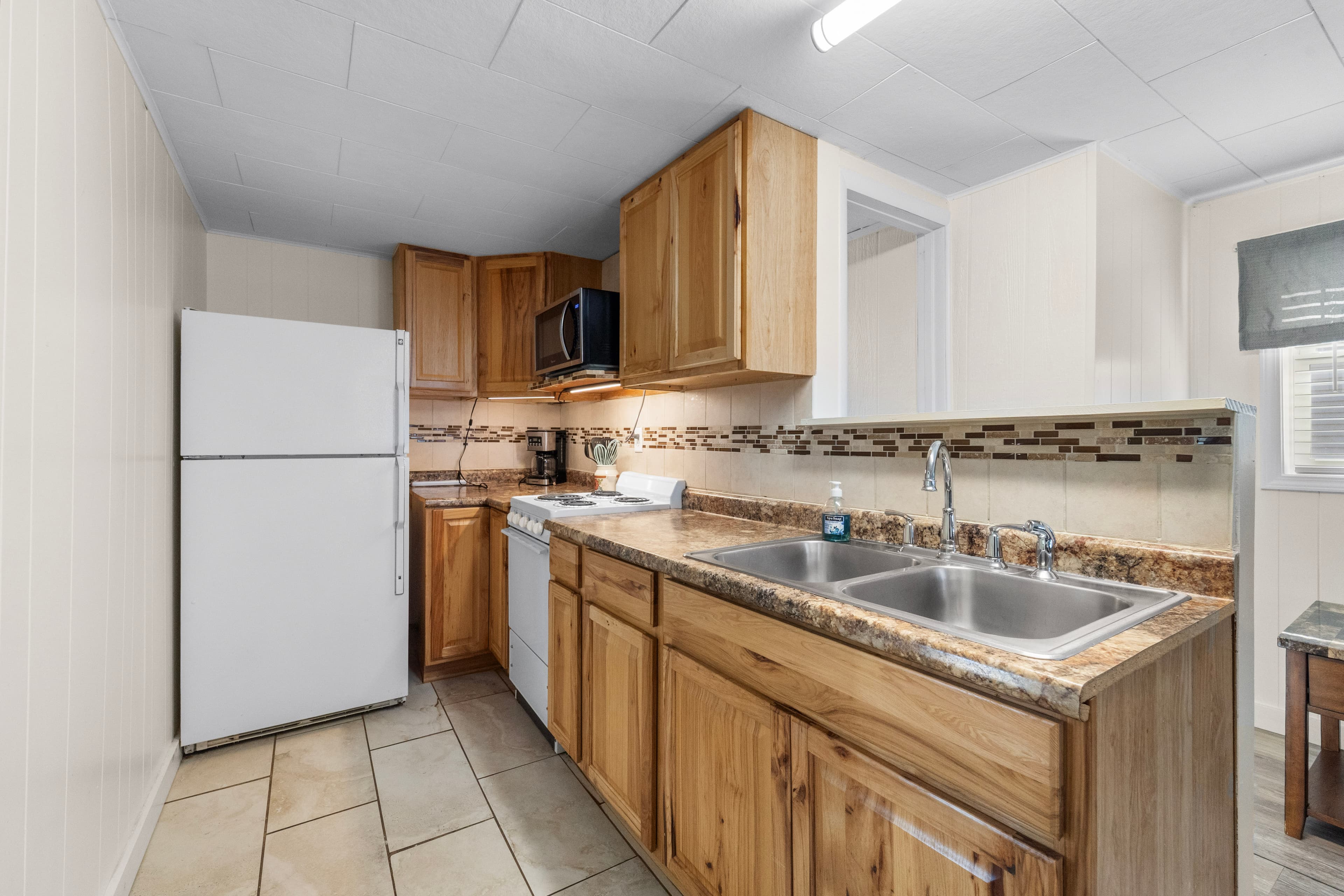 A modern kitchen featuring wooden cabinets, a double sink, a white refrigerator, and a tile floor.