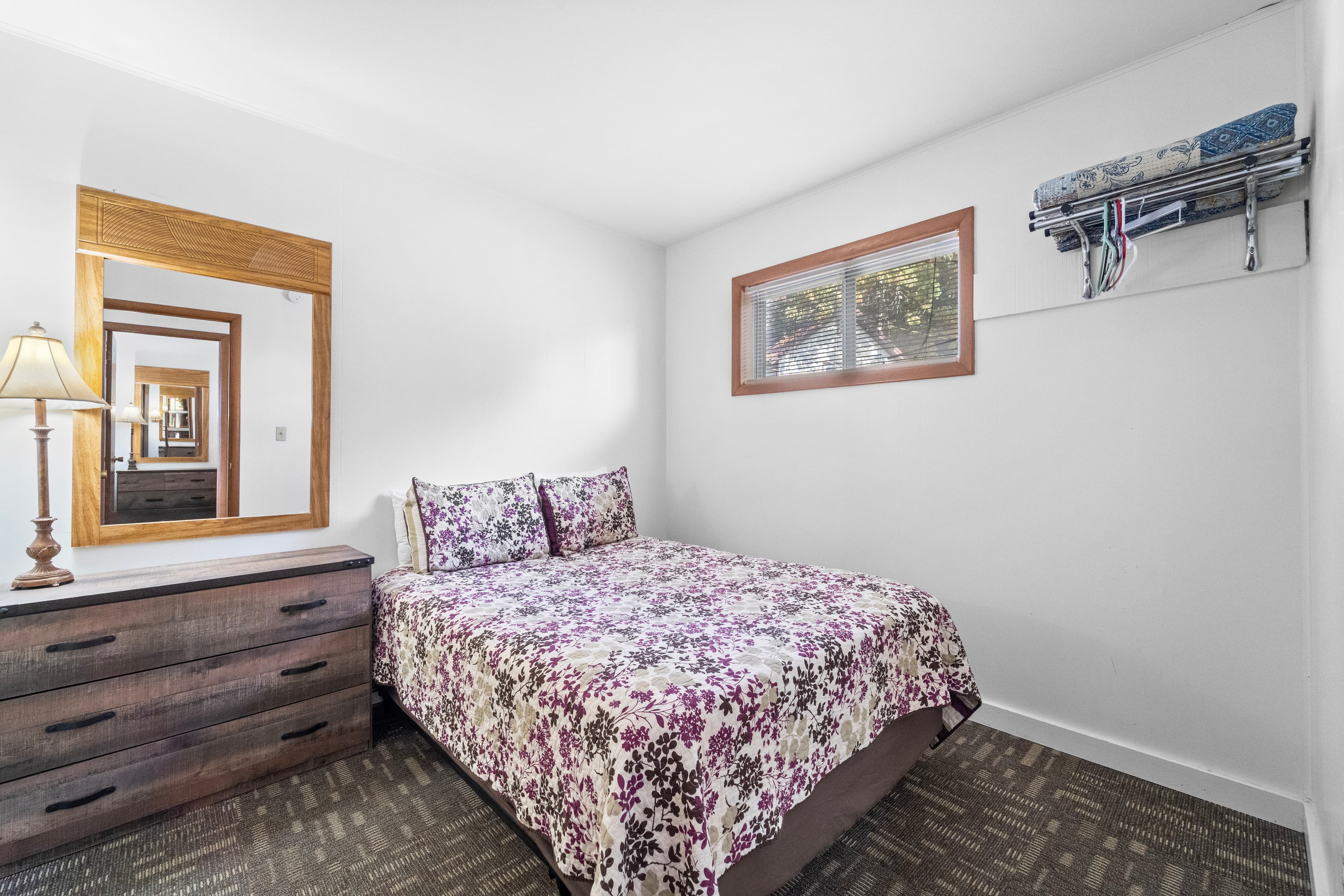 A cozy bedroom featuring a queen bed with a floral comforter, a wooden dresser, and a mirror.
