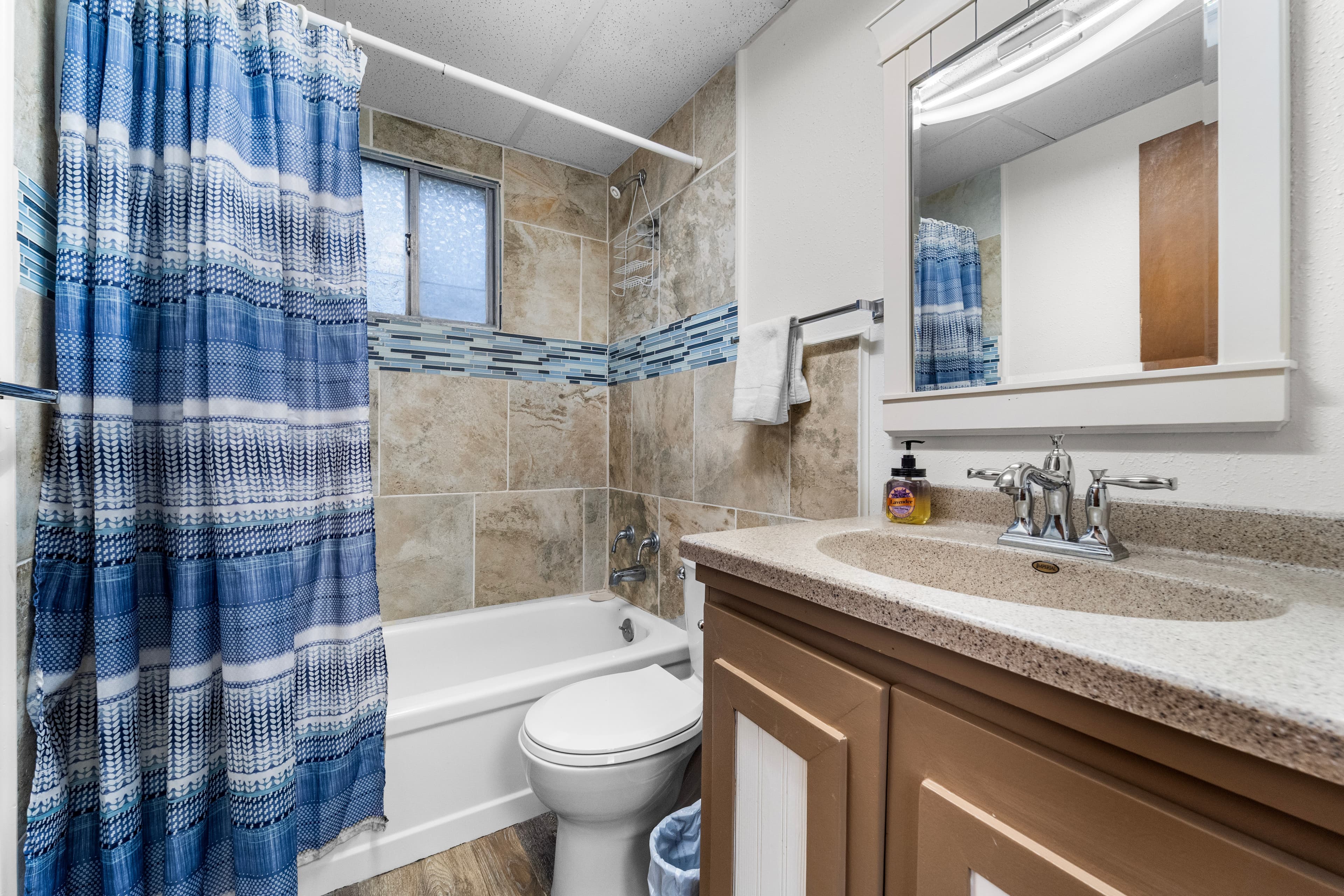 A modern bathroom featuring a bathtub, toilet, and vanity with a mirror, accented by a blue and white shower curtain.
