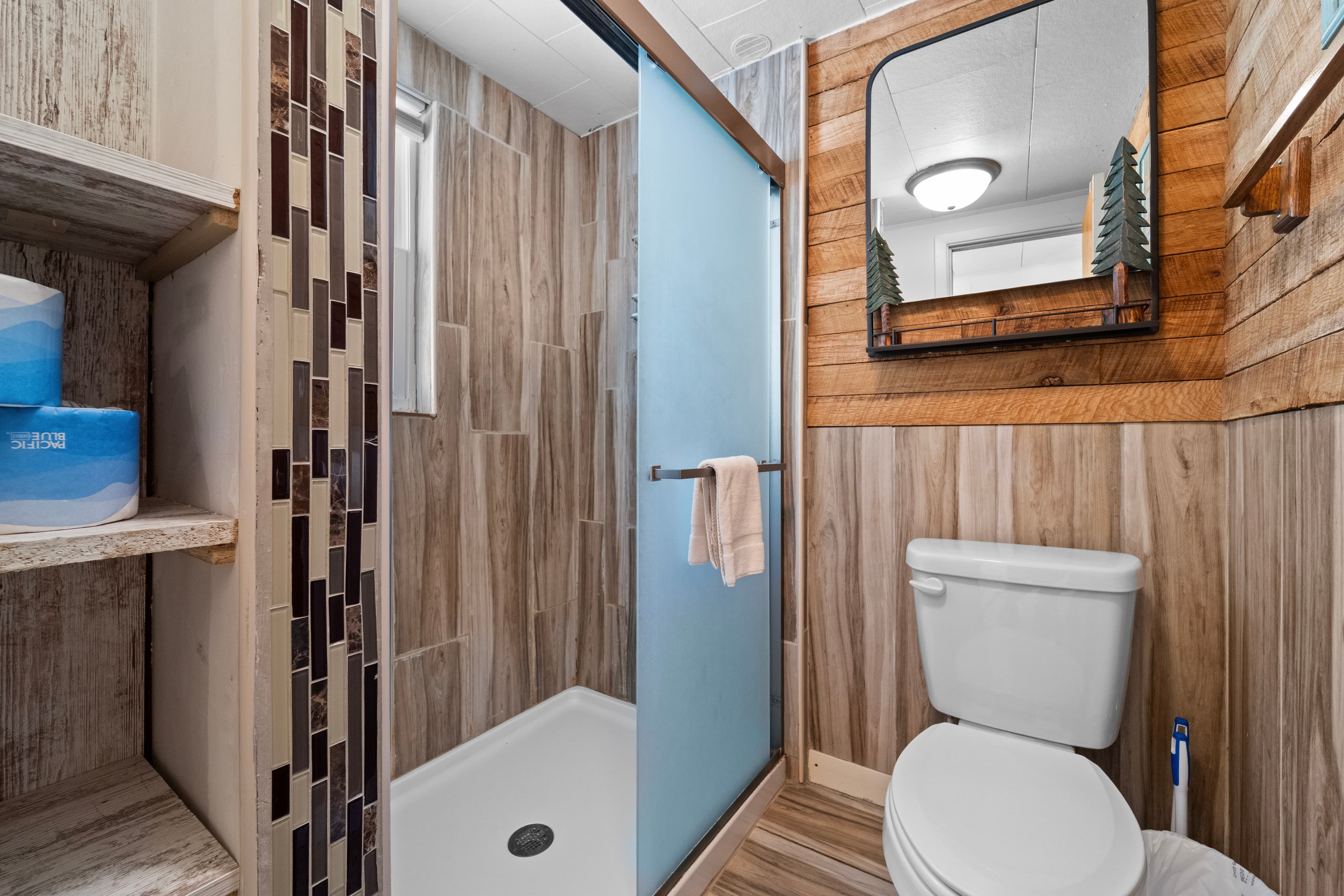 A modern bathroom featuring a glass shower, wooden accents, and a clean white toilet.