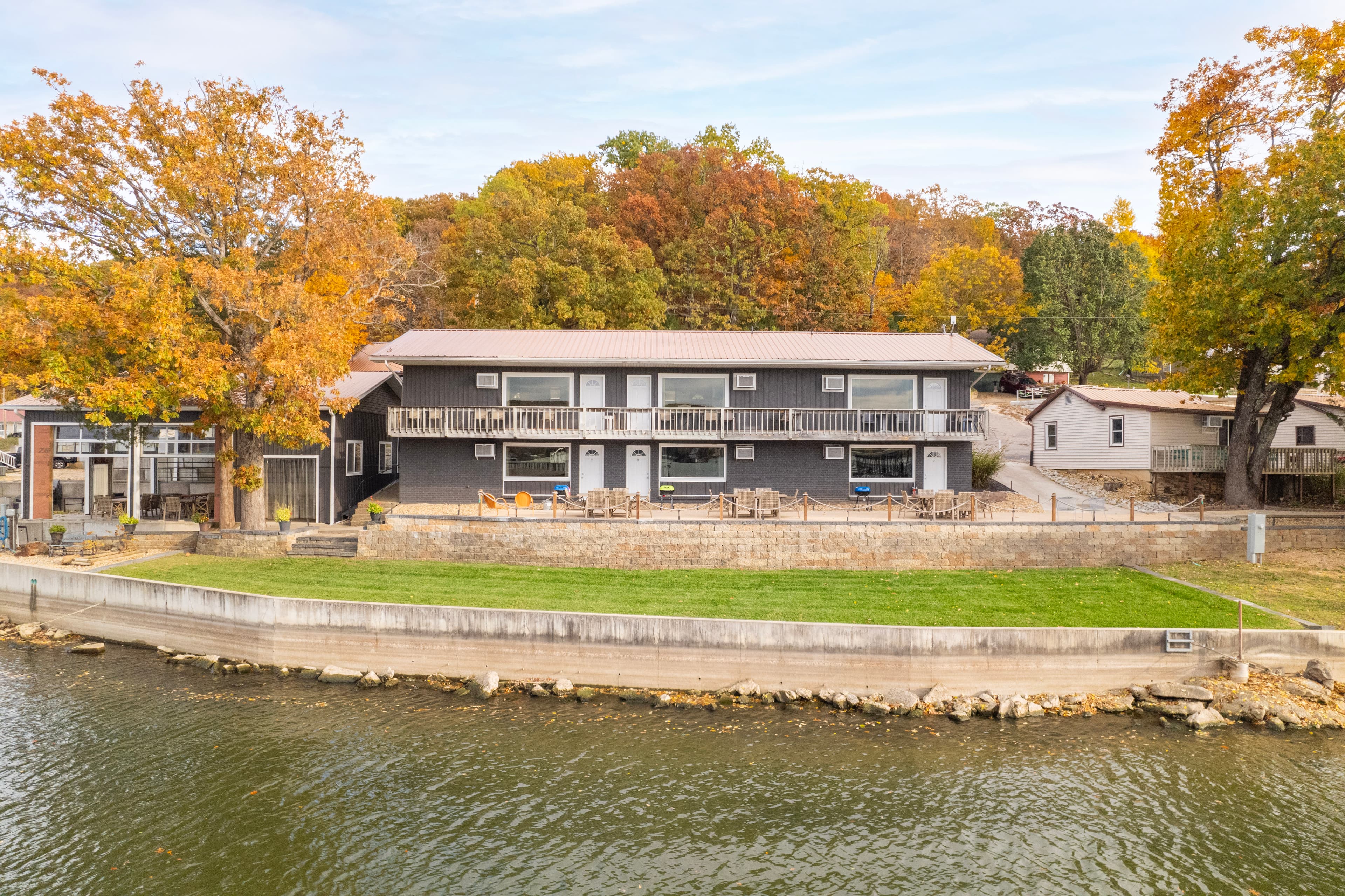 A lakeside building surrounded by autumn trees and a grassy area.
