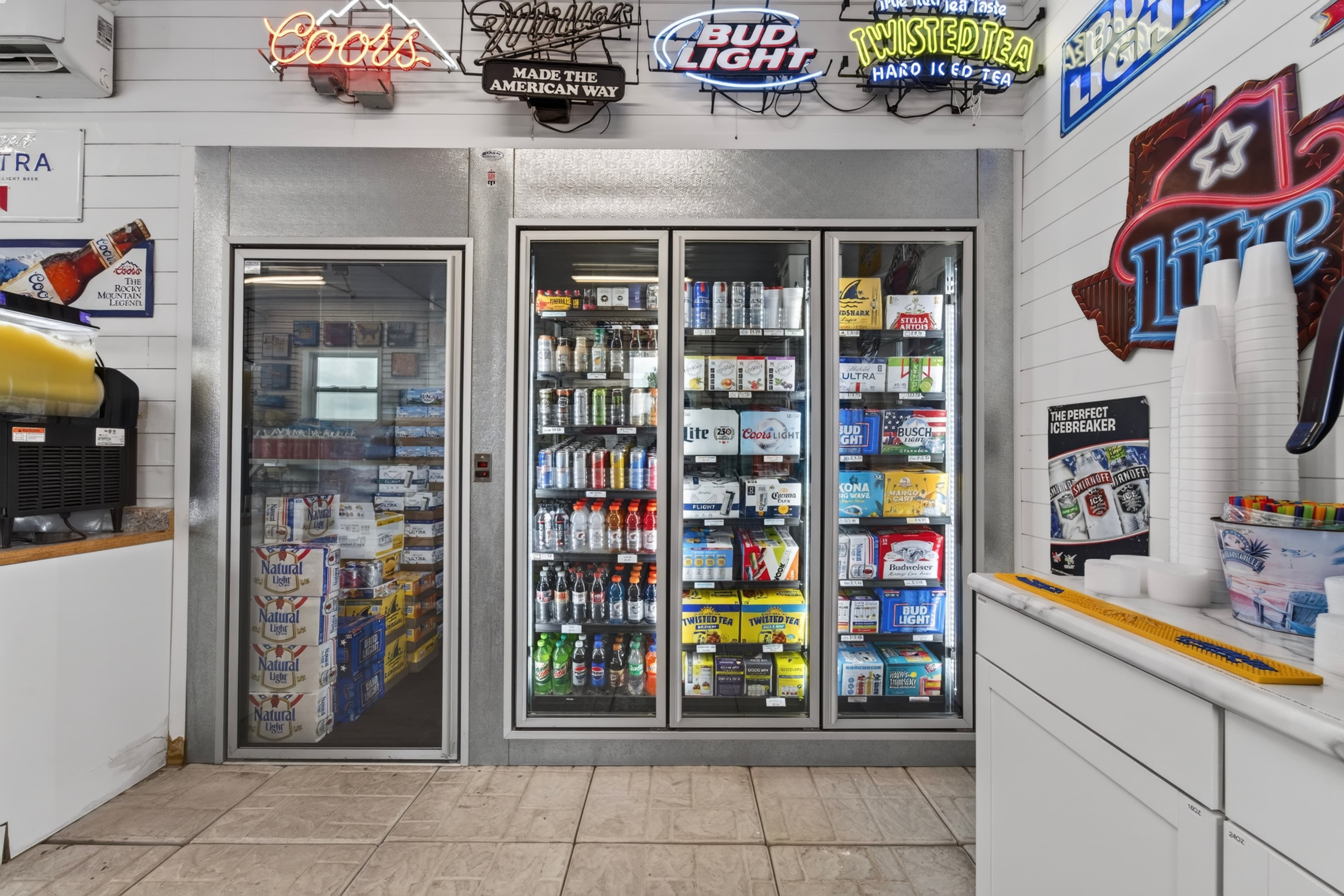 A convenience store cooler displays various beverages with neon signs overhead.