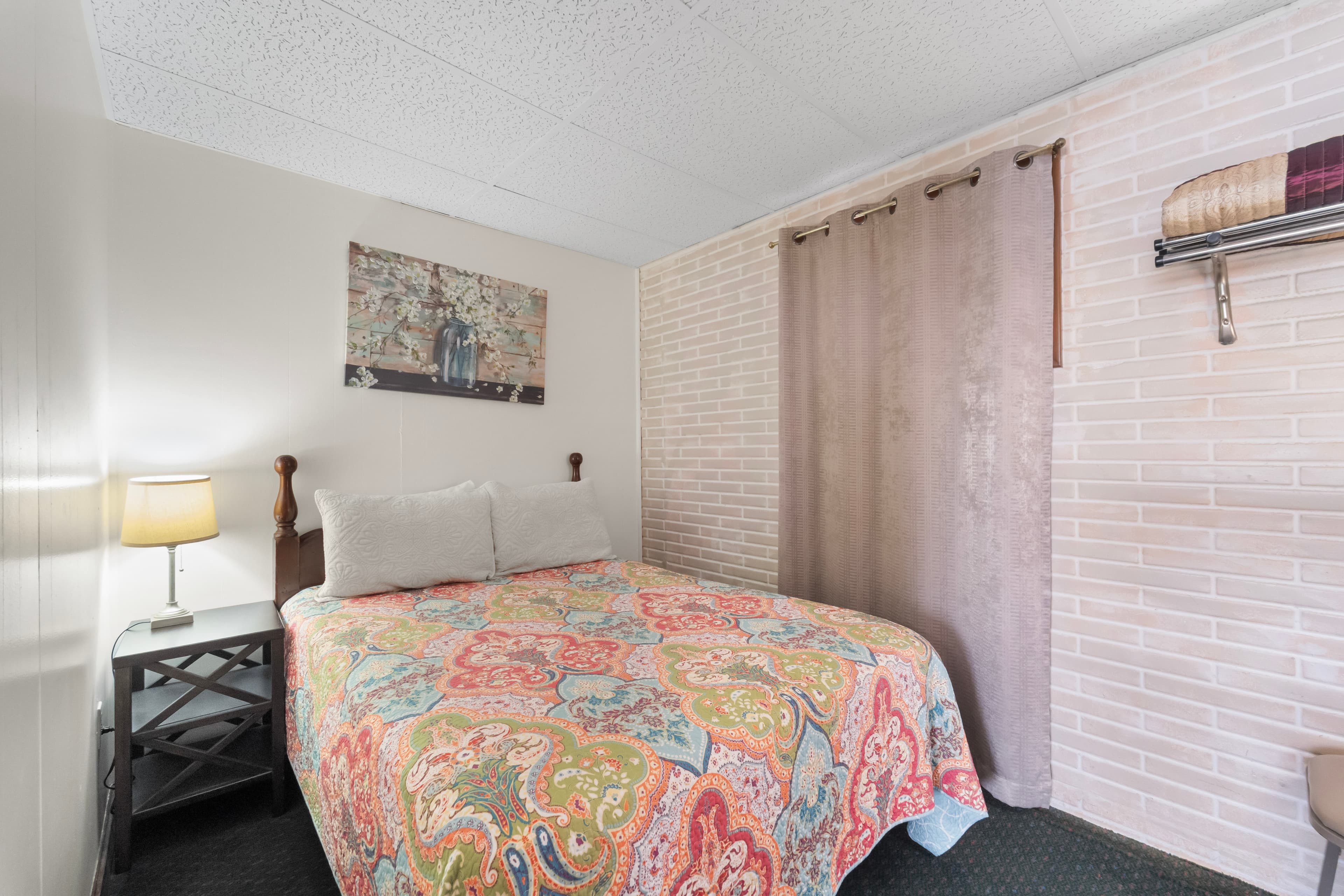 Cozy bedroom featuring a colorful patterned bedspread, nightstand with a lamp, and soft lighting.