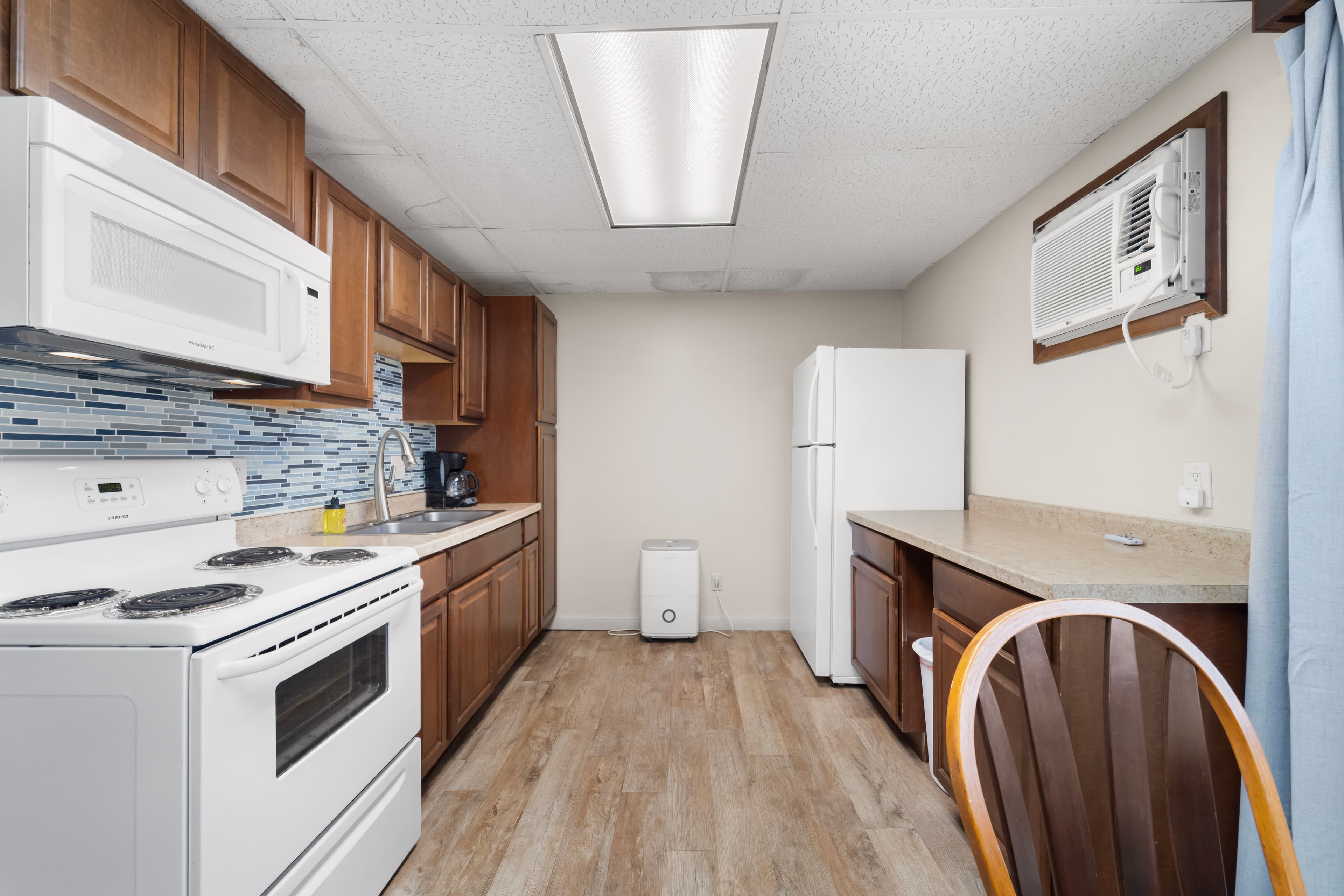 Modern kitchen featuring wooden cabinets, a white stove, microwave, and refrigerator, along with a light countertop and an air conditioning unit.