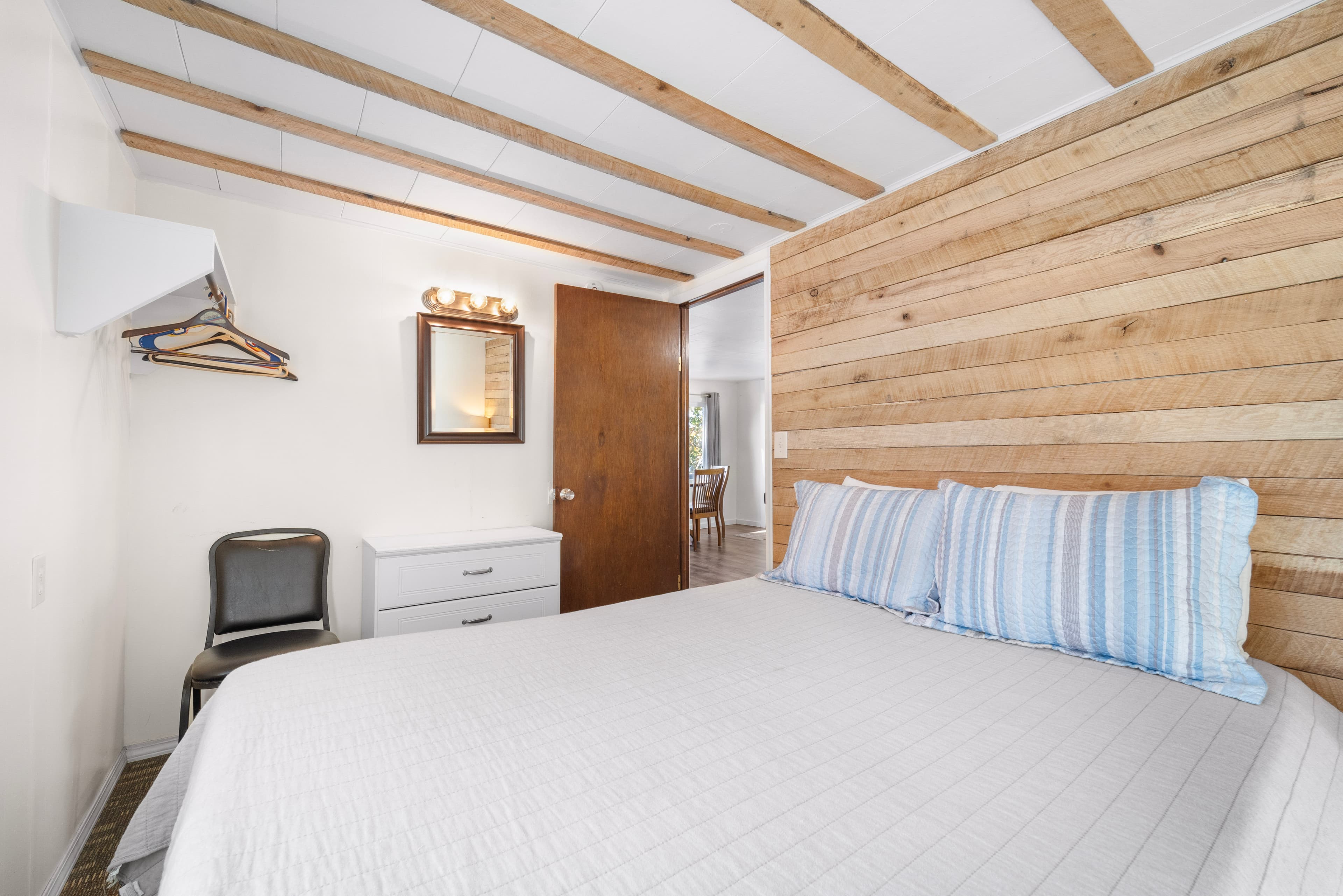 A cozy bedroom featuring a wooden accent wall, a double bed with blue striped pillows, and simple furnishings.