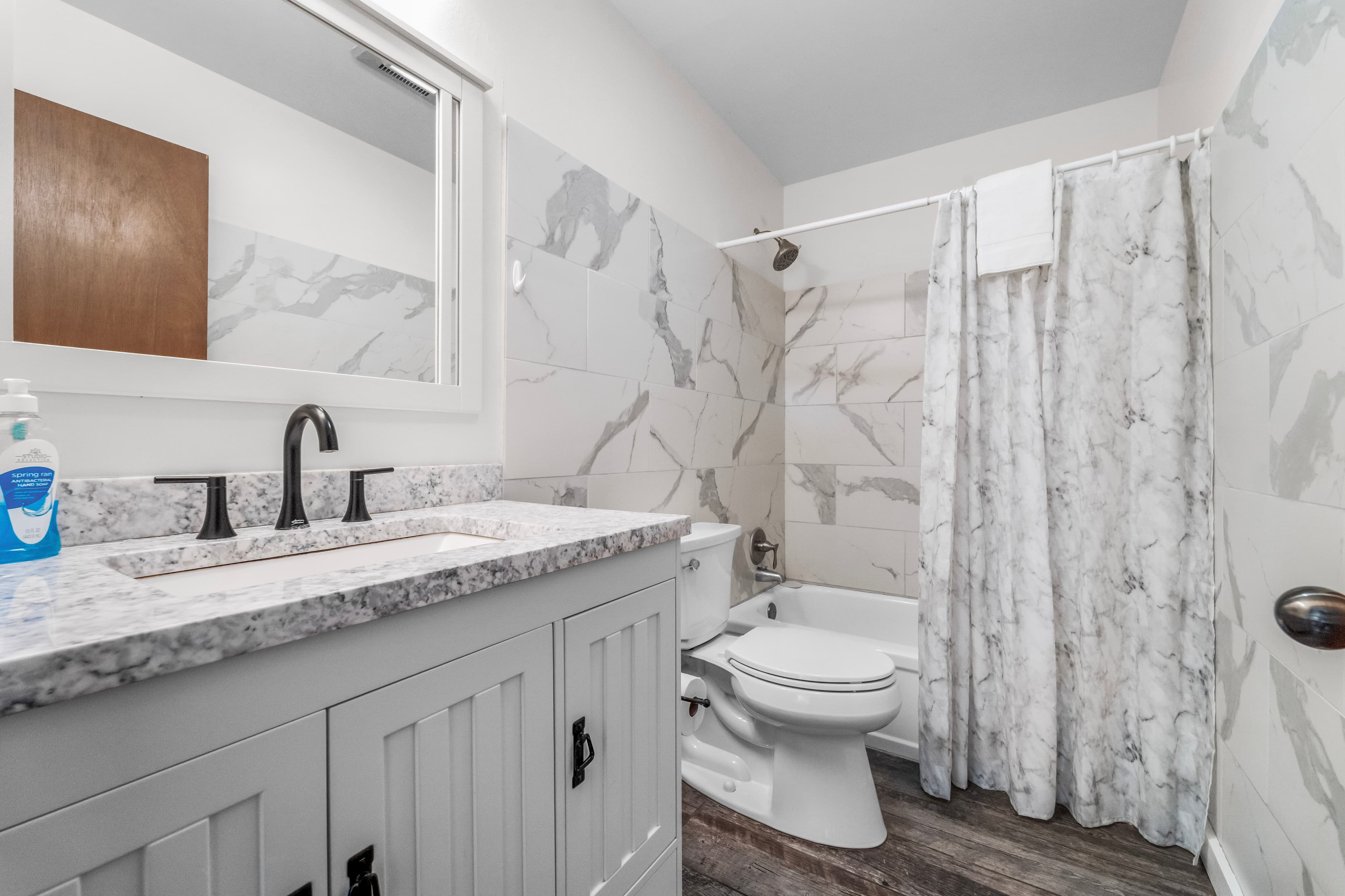 A modern bathroom featuring a marble countertop, a shower with a patterned curtain, and a clean toilet.