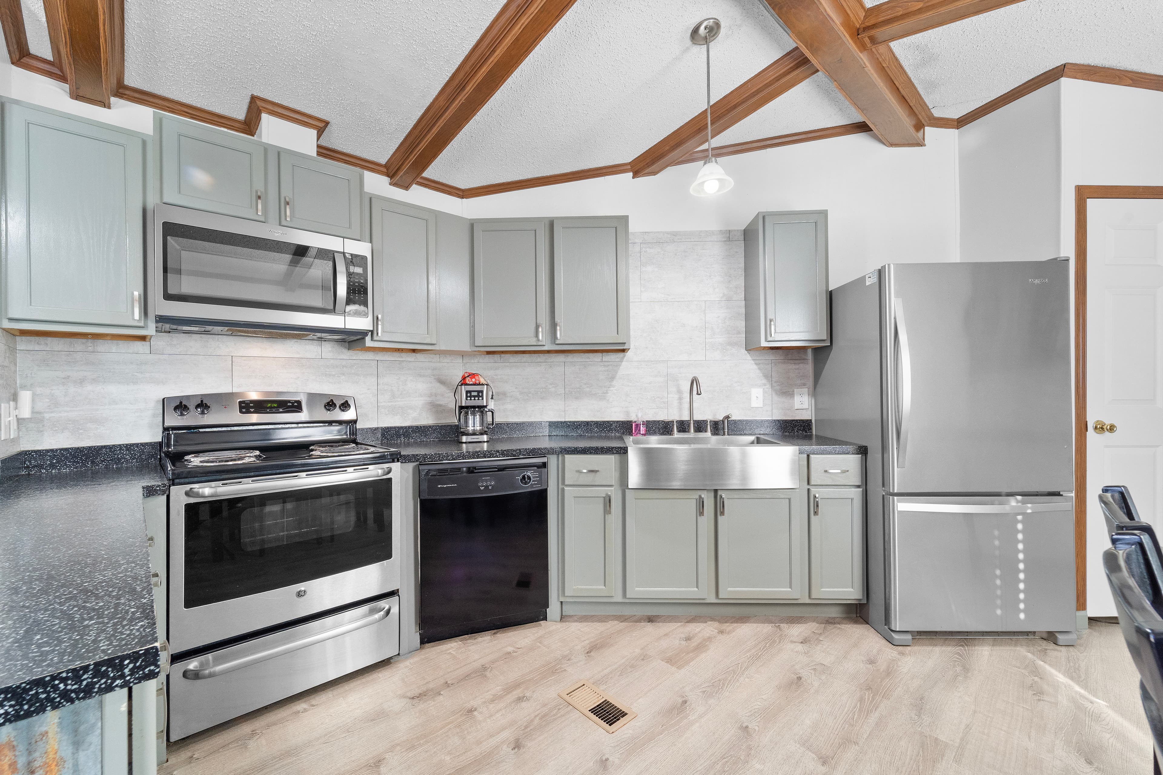 Modern kitchen with gray cabinets, stainless steel appliances, and wooden beams.