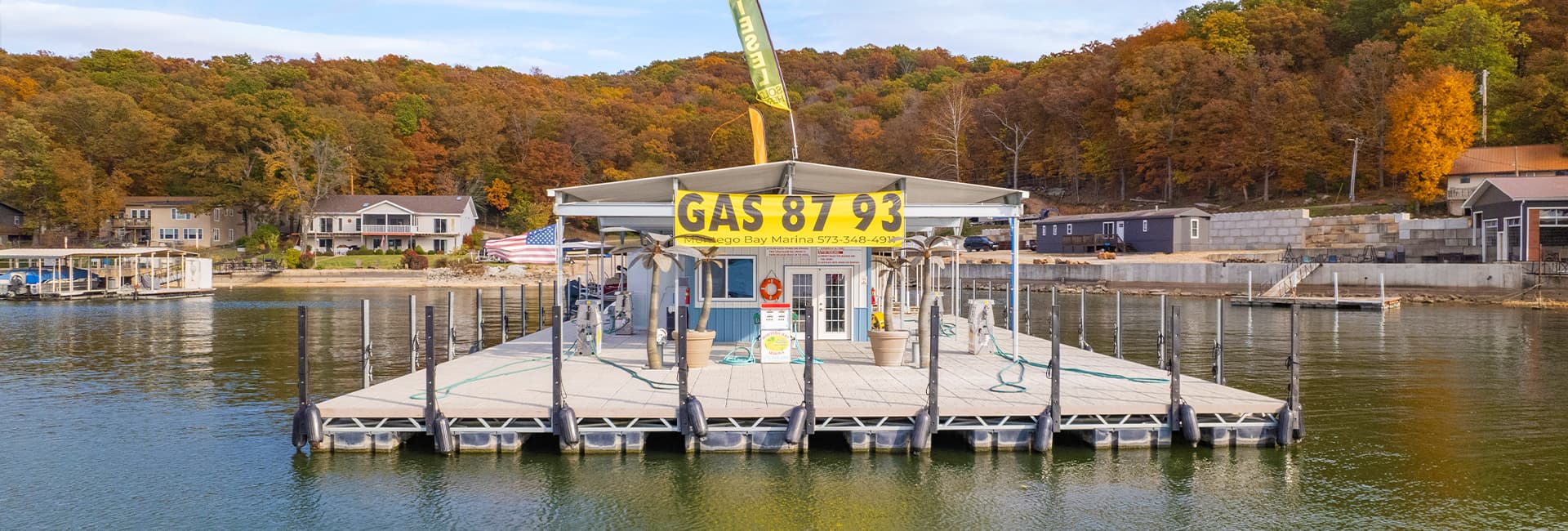 A gas station on a dock, surrounded by autumn-colored trees and water.
