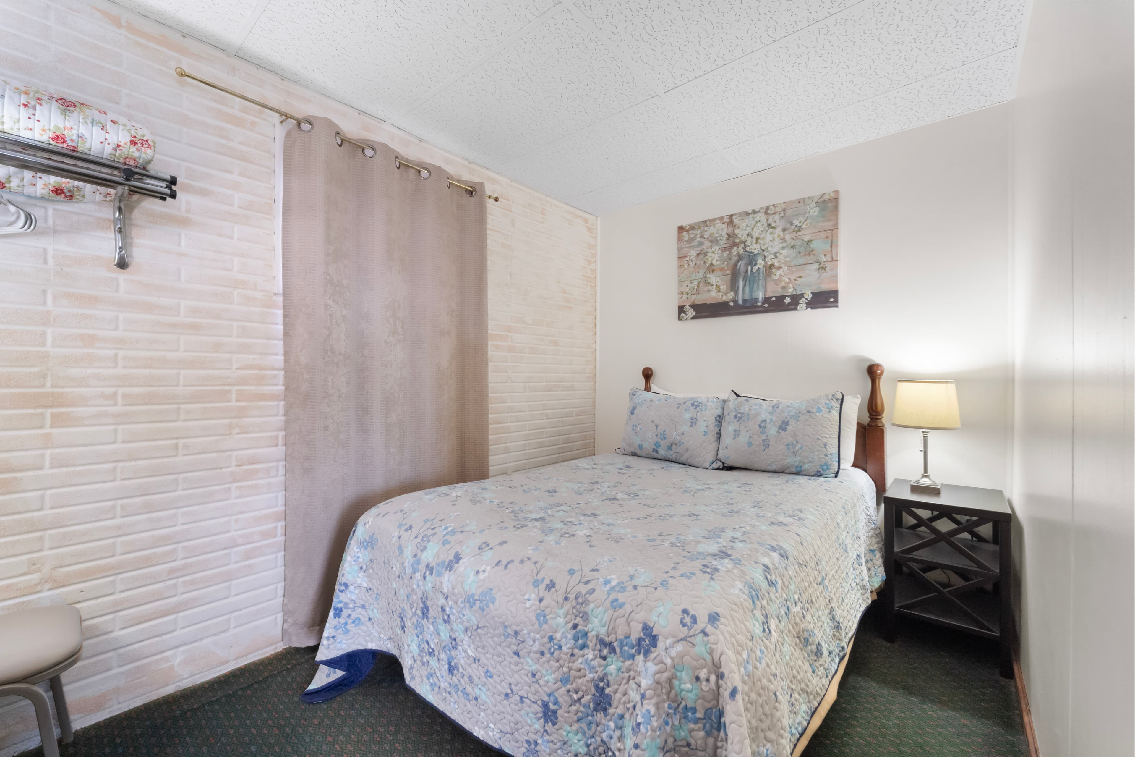A cozy bedroom featuring a double bed with a floral quilt, a bedside lamp, and a curtain partition.