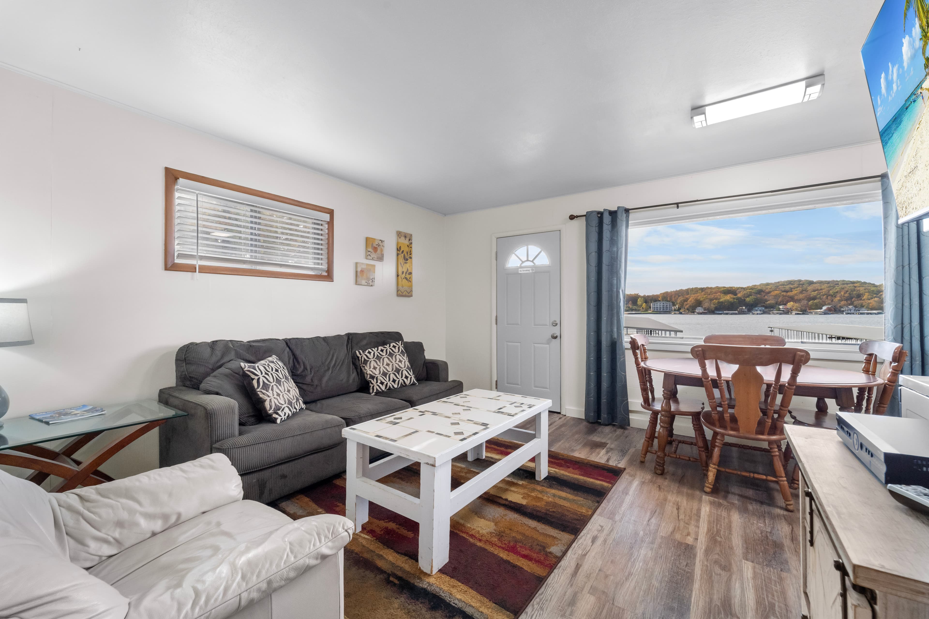 A cozy living room with a sofa, dining area, and door leading to a scenic view outside.