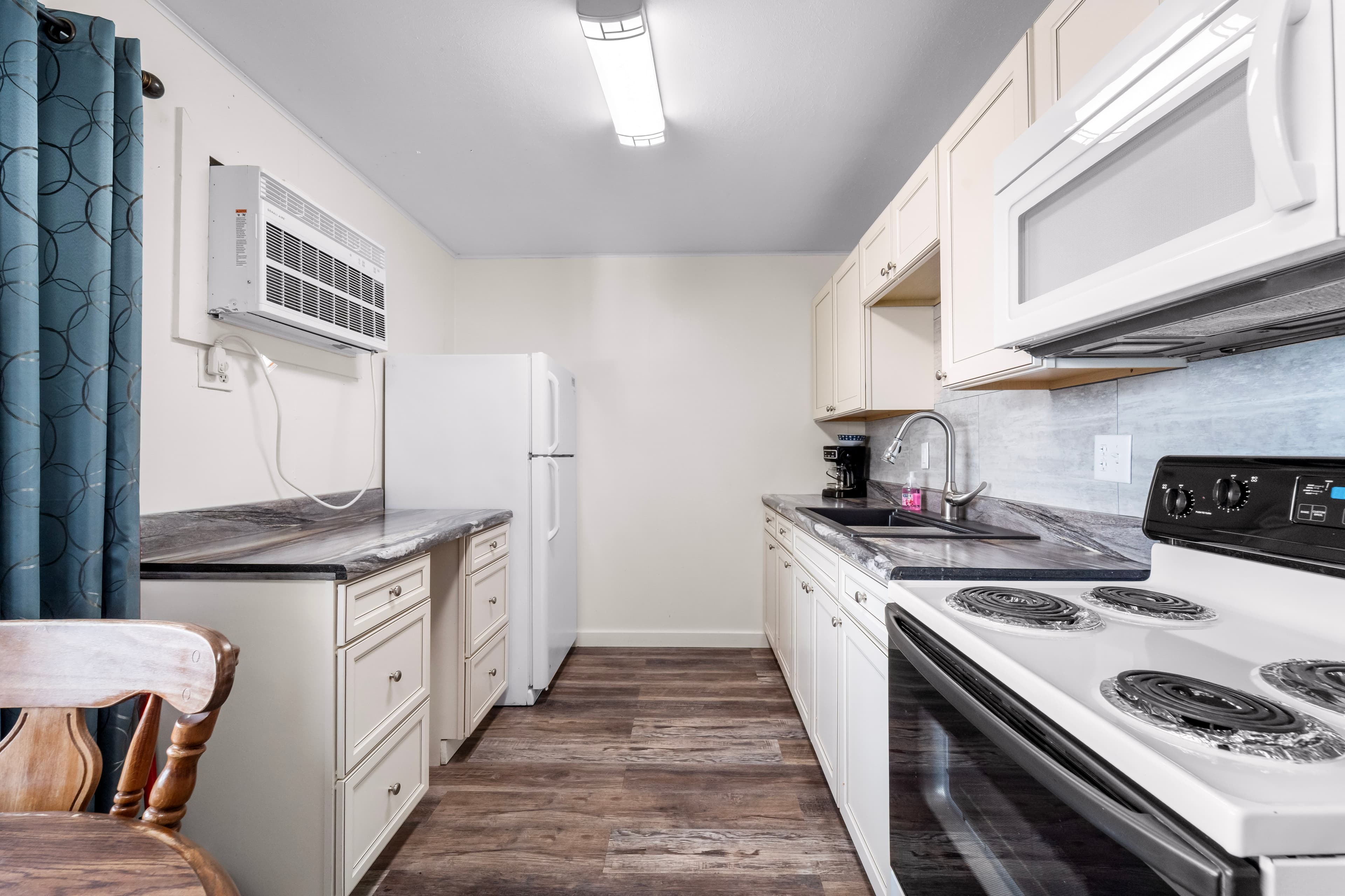 A modern kitchen featuring white cabinetry, a black stove, a microwave, and a refrigerator.