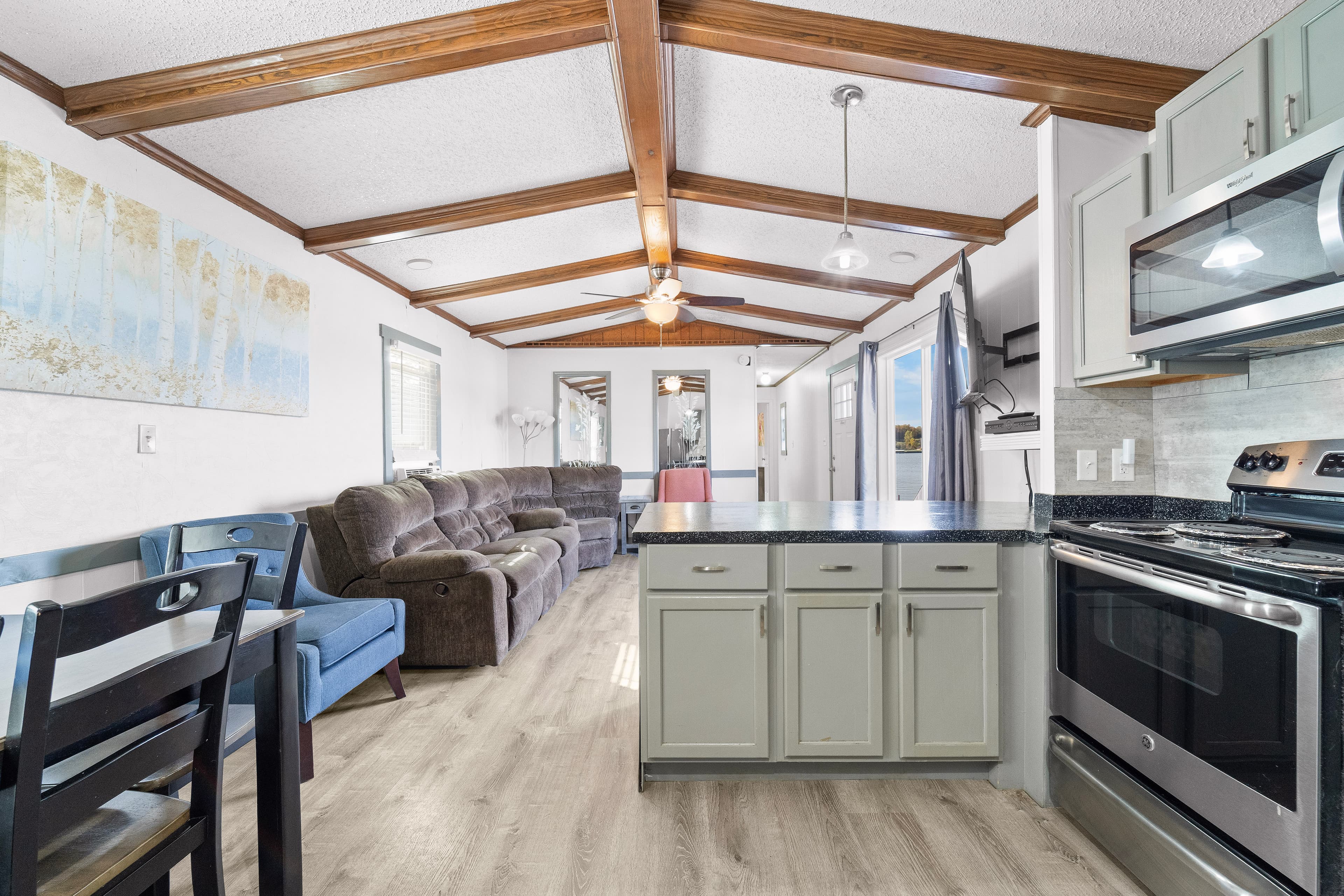 A modern living space featuring a kitchen island, sofa seating, and wooden beams on the ceiling.