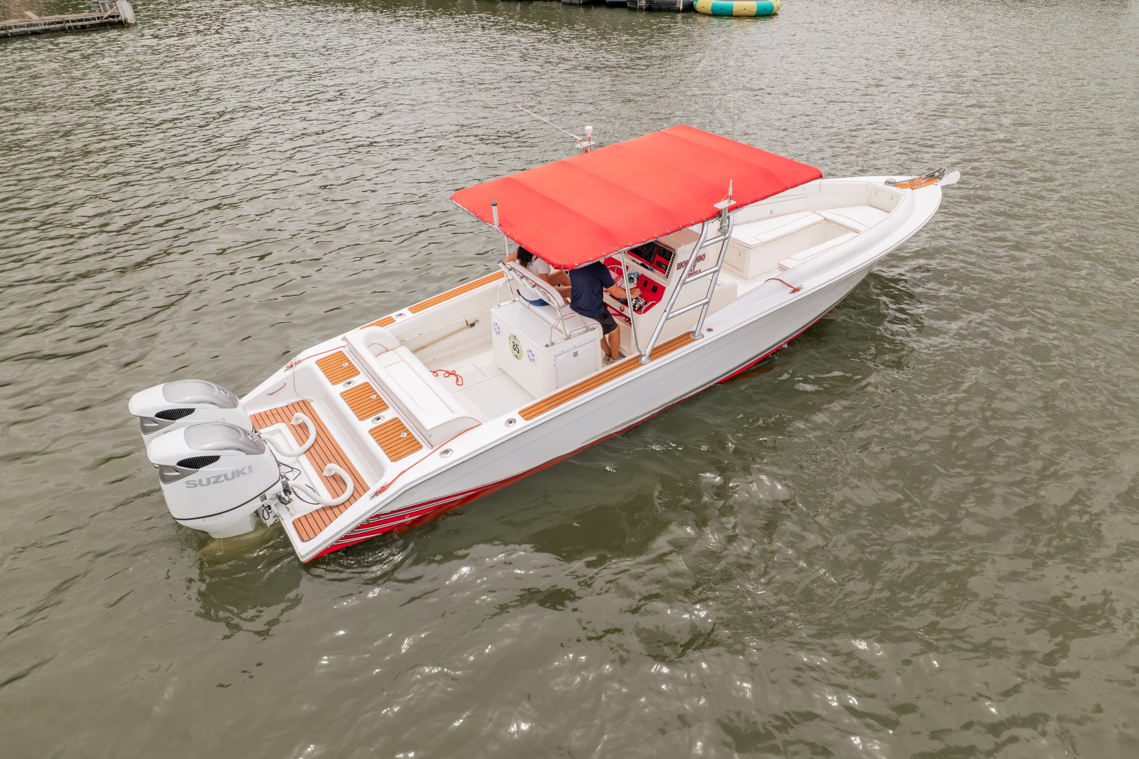A white motorboat with a red canopy is anchored on calm water, with a person at the controls.