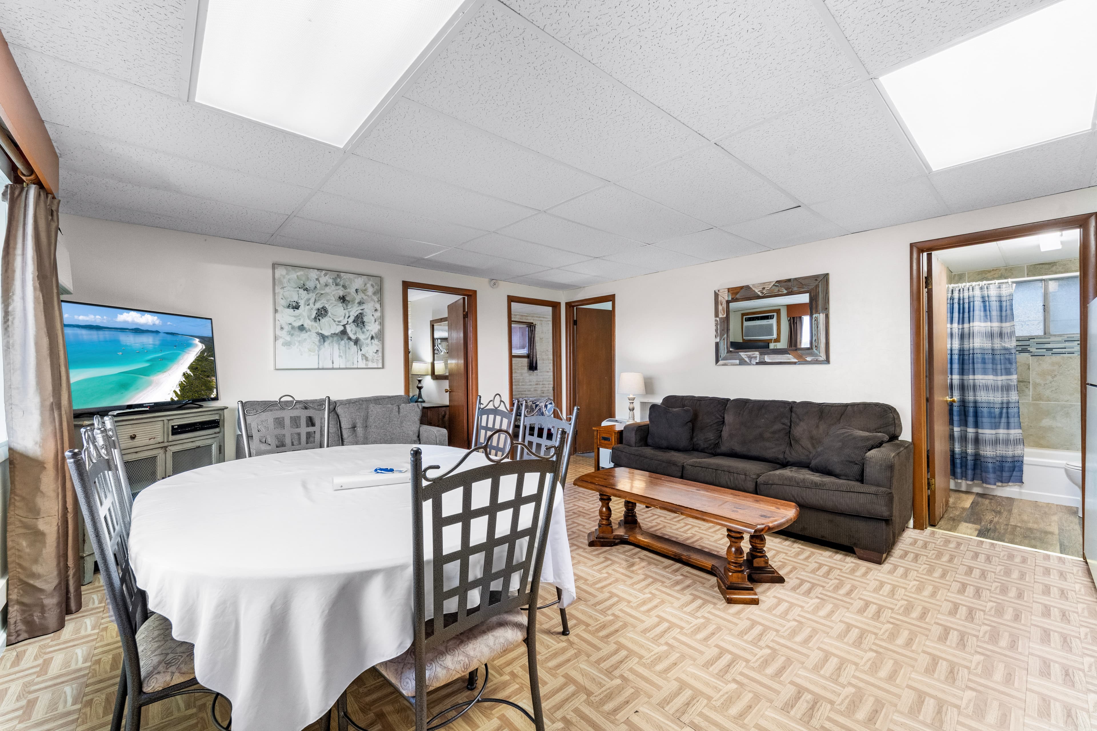 A cozy living and dining area featuring a table, chairs, a sofa, and a TV, with access to a bathroom.