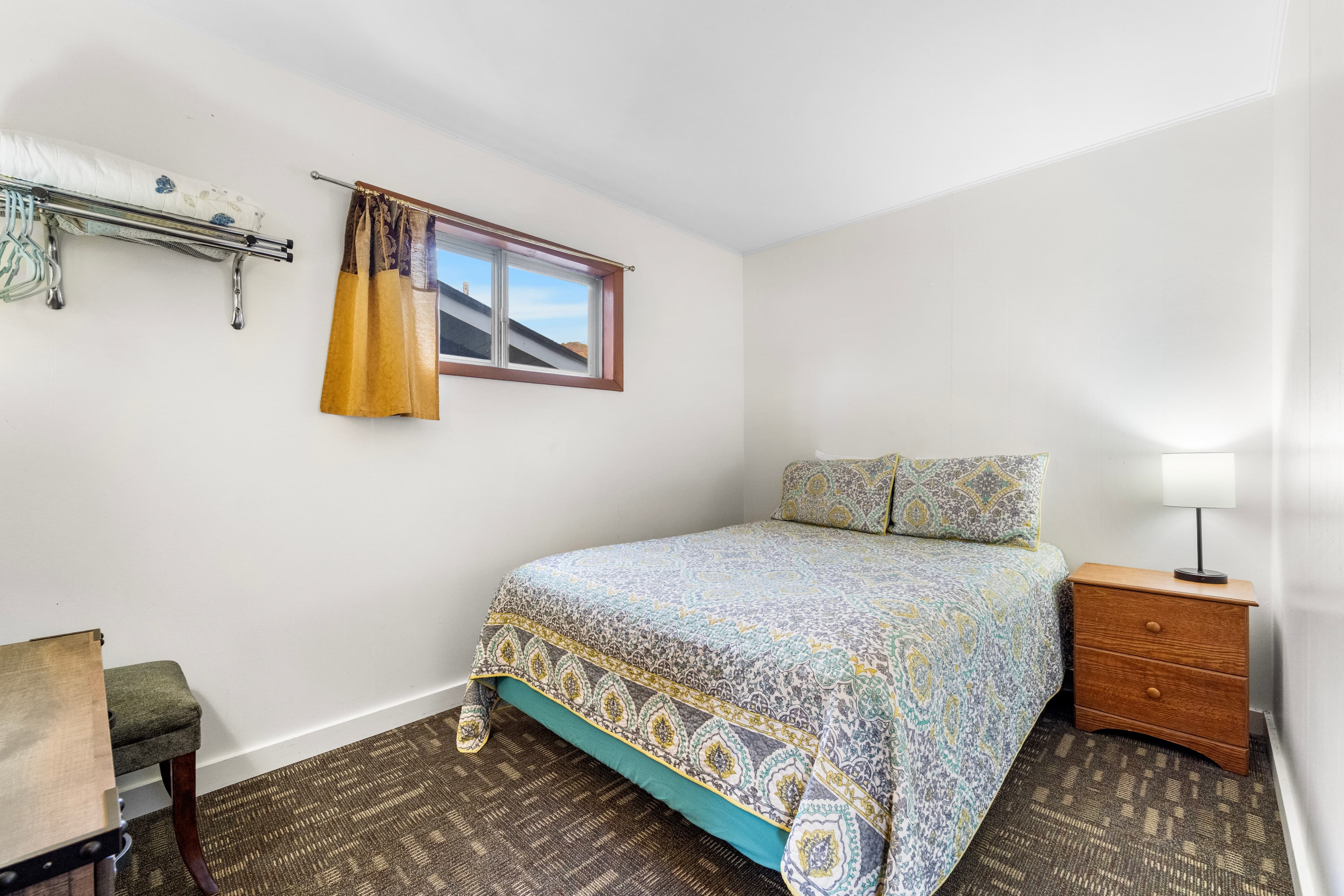 Cozy bedroom featuring a bed with a patterned blanket, a nightstand with a lamp, and a small desk.