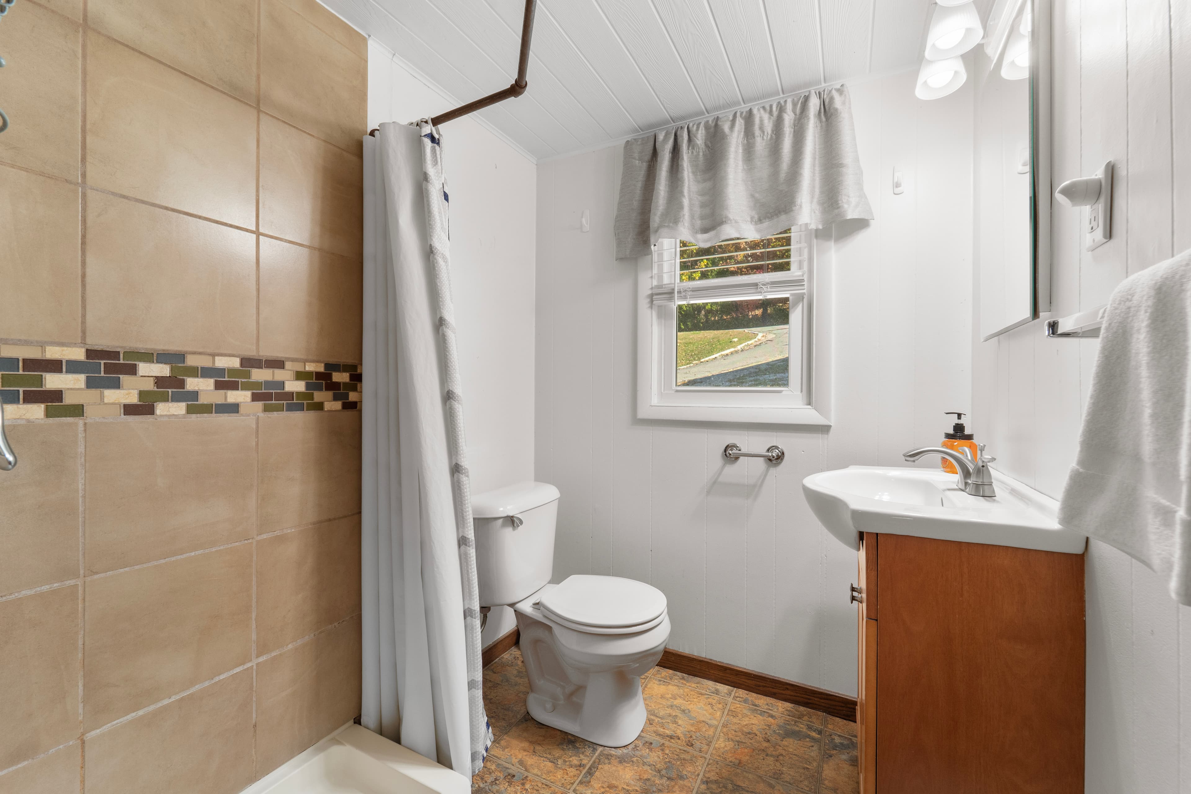 A clean bathroom featuring a shower, toilet, and sink with a window for natural light.
