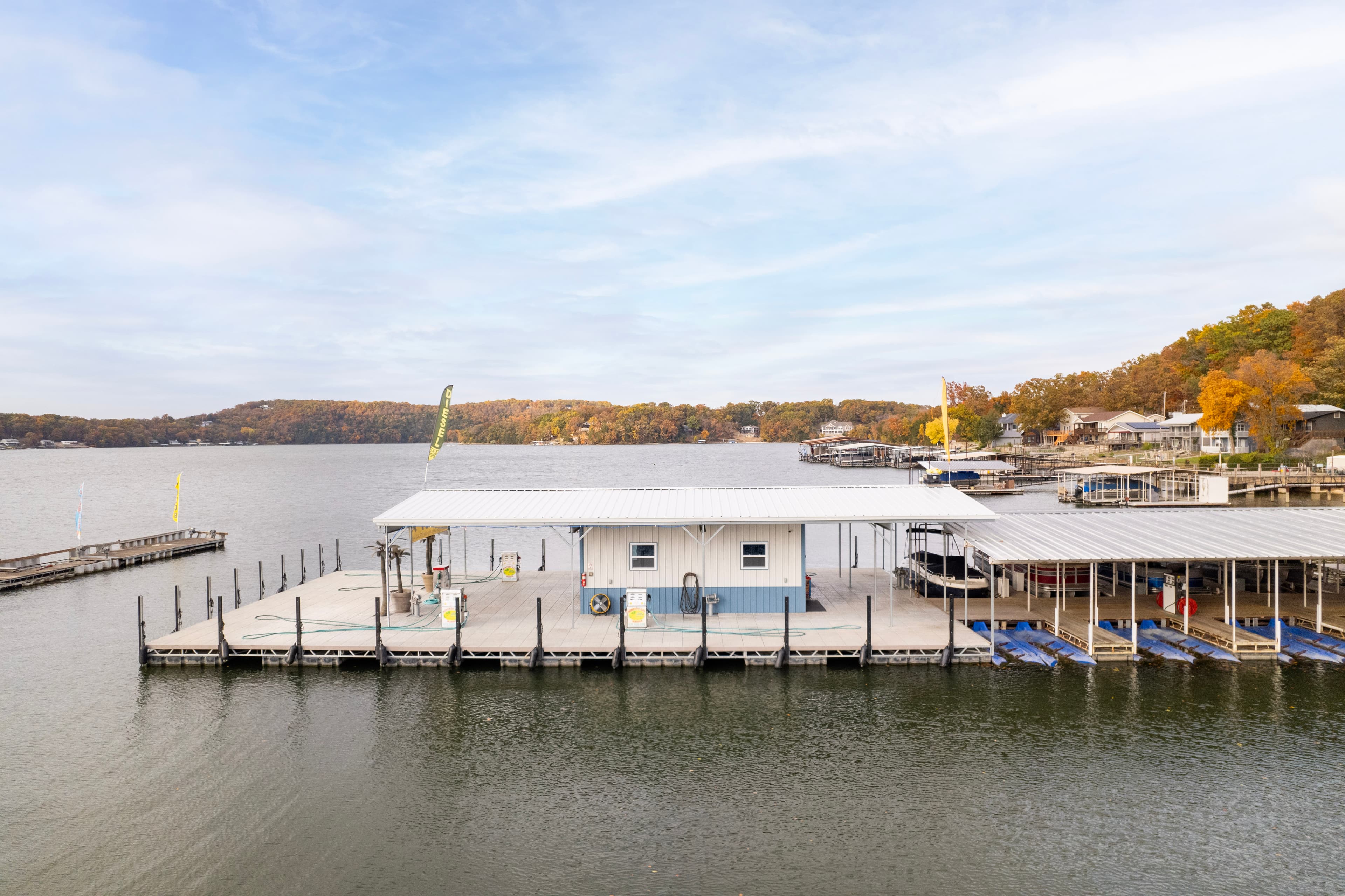 Aerial view of a lakeside marina with a boat dock and autumn foliage in the background.