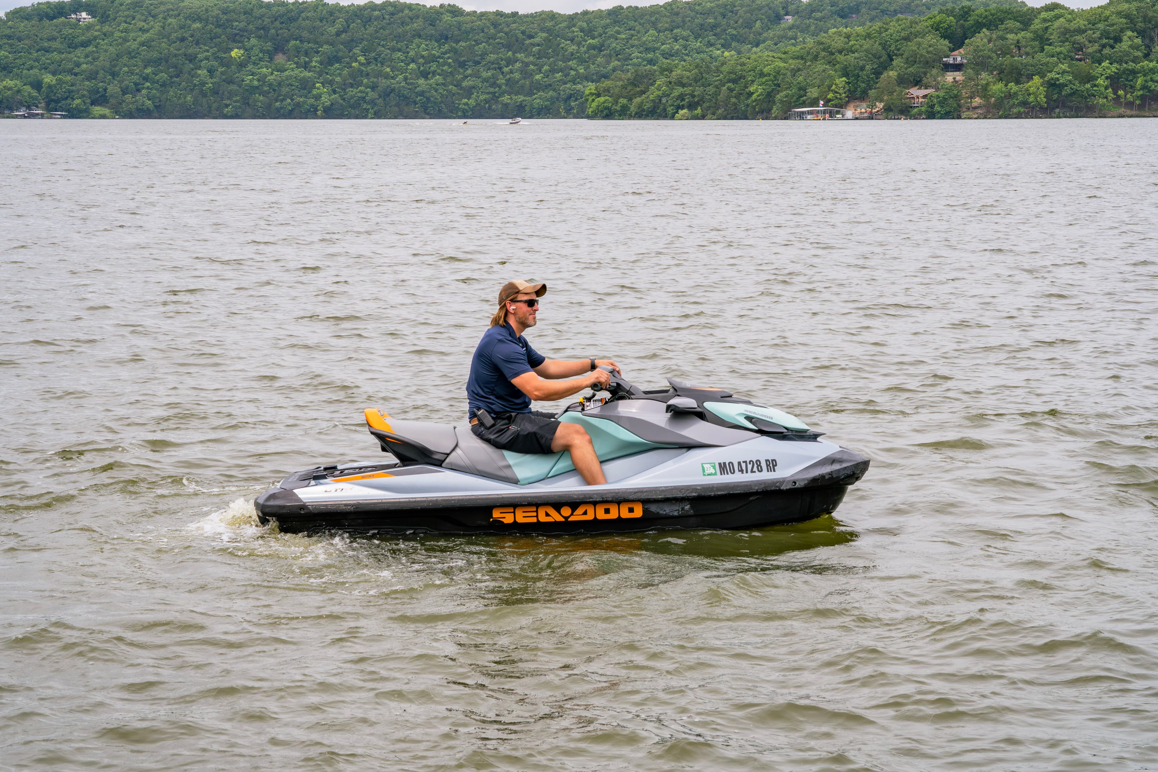 A person riding a Sea-Doo jet ski on a calm lake surrounded by green hills.