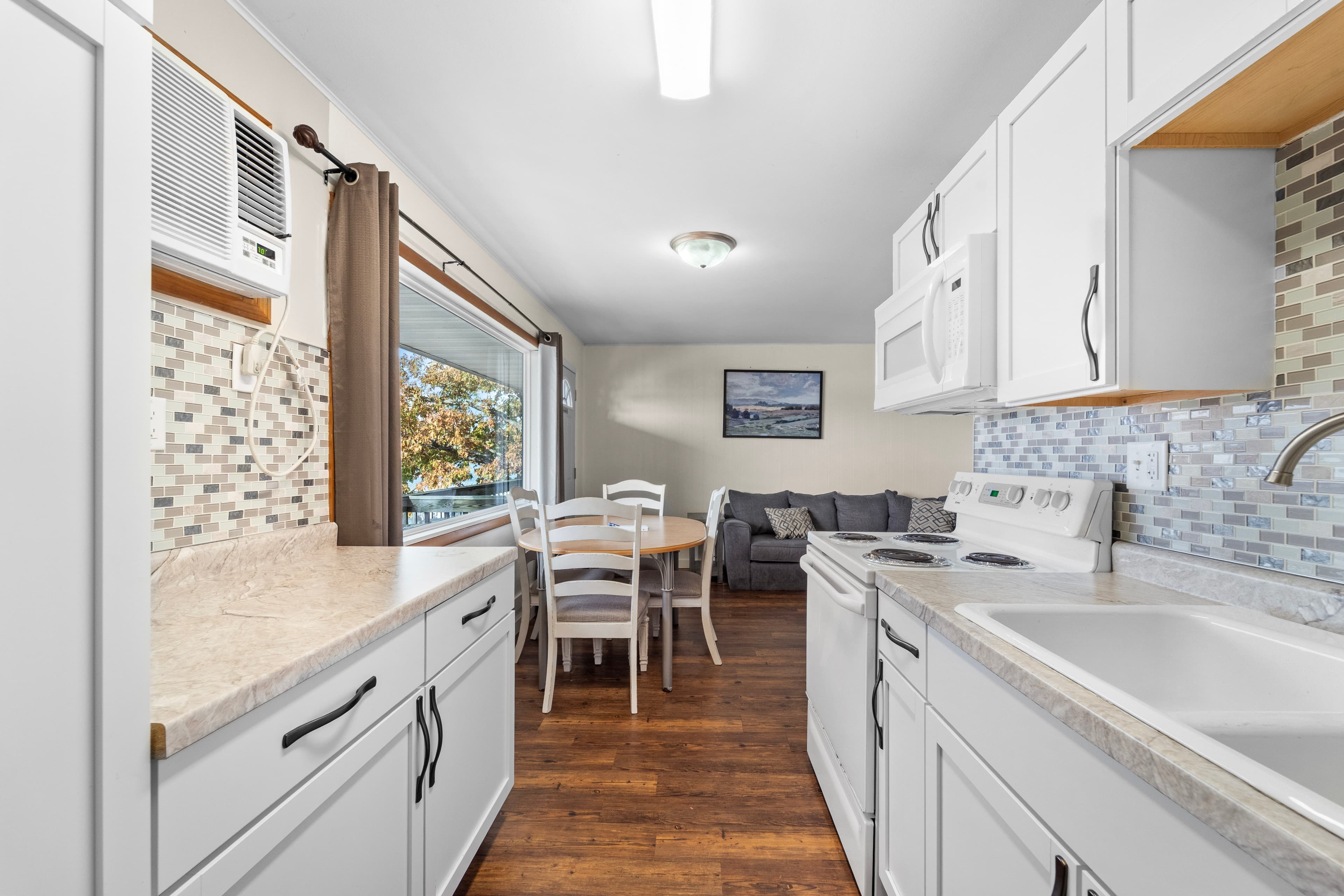 Bright kitchen with white cabinetry, a dining area, and a view of a cozy living room.