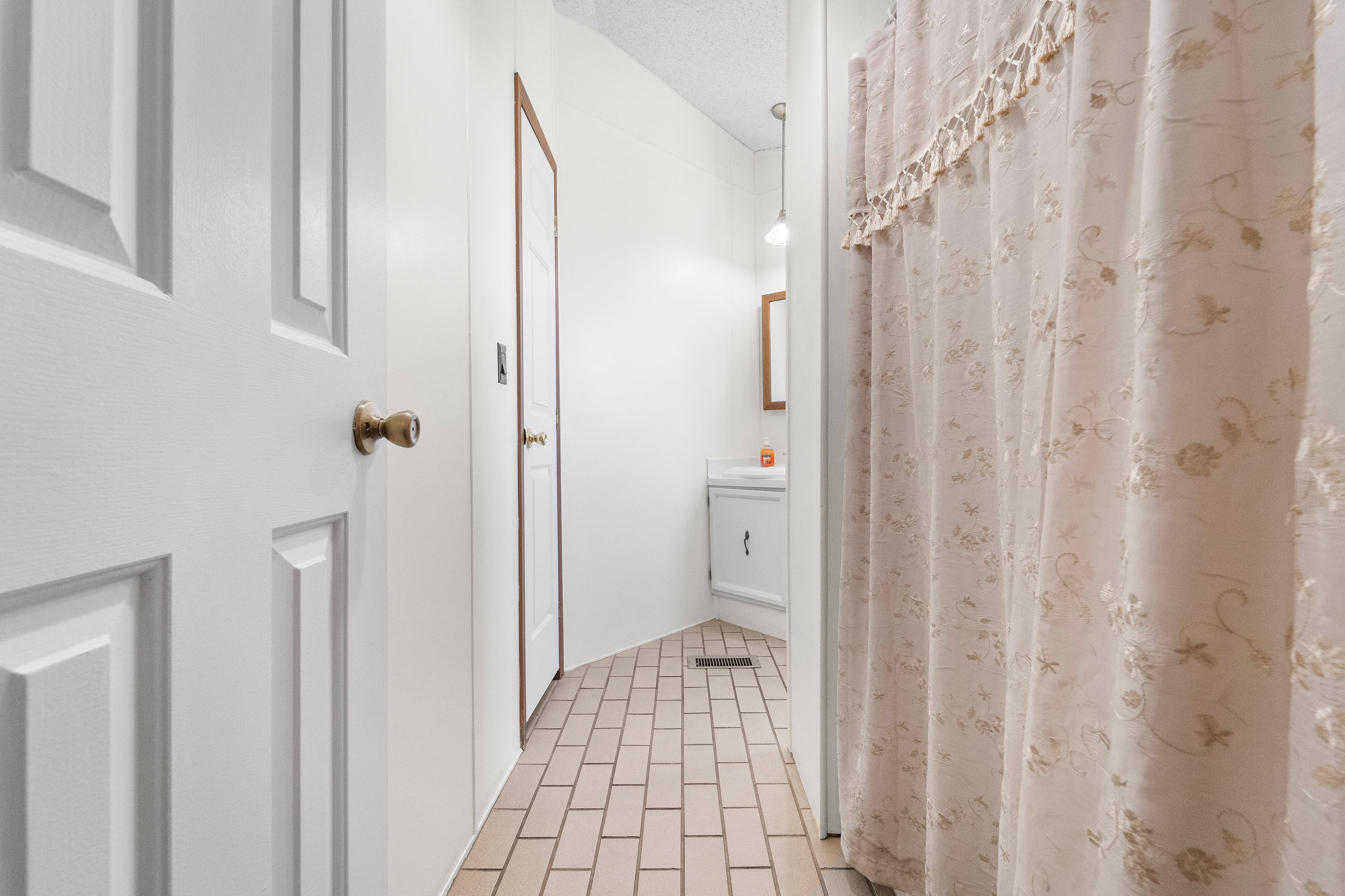 A bathroom doorway with a floral shower curtain and beige tiled floor.