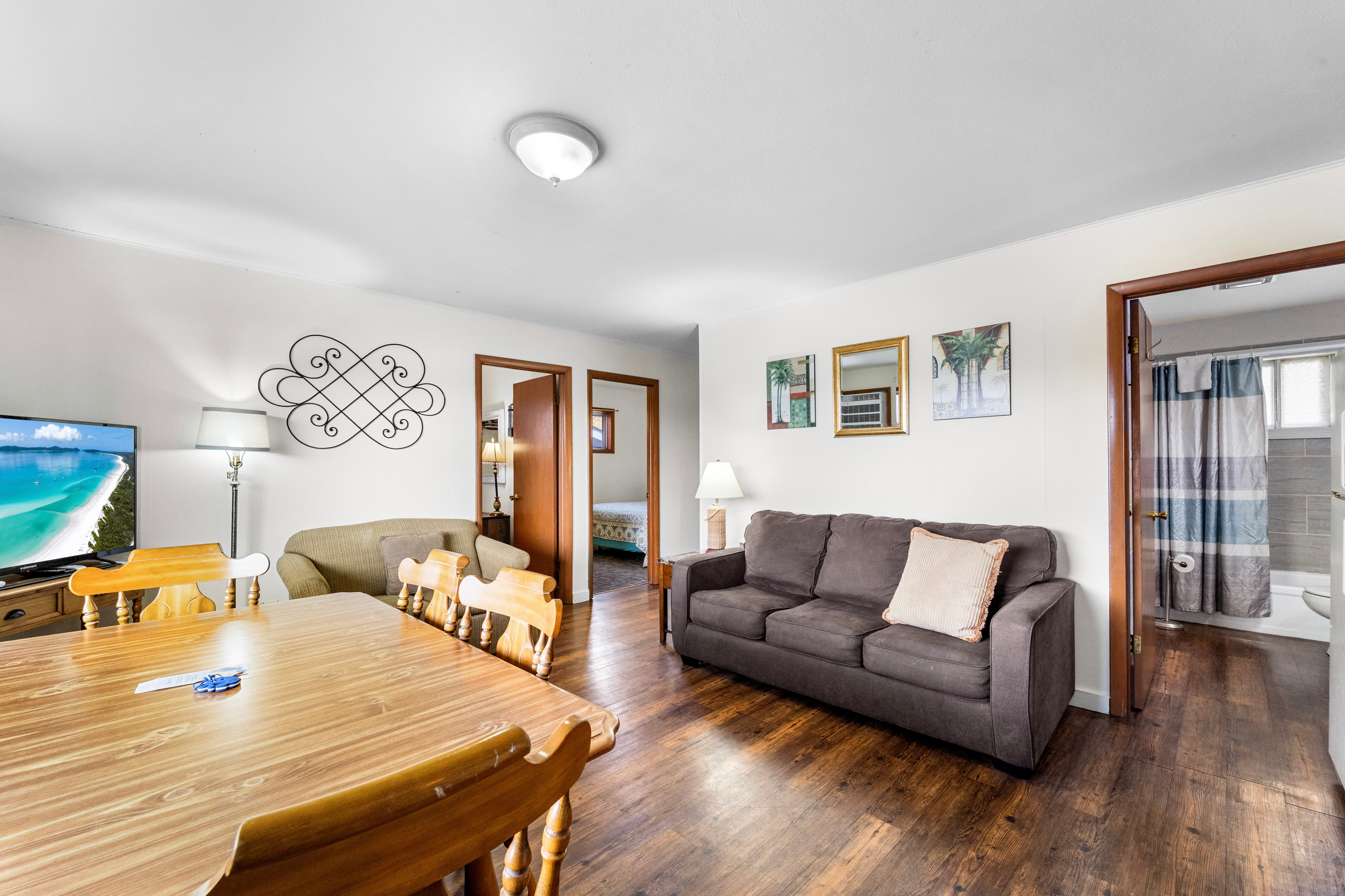 A cozy living room with a sofa, dining table, and a television, leading to a bathroom.