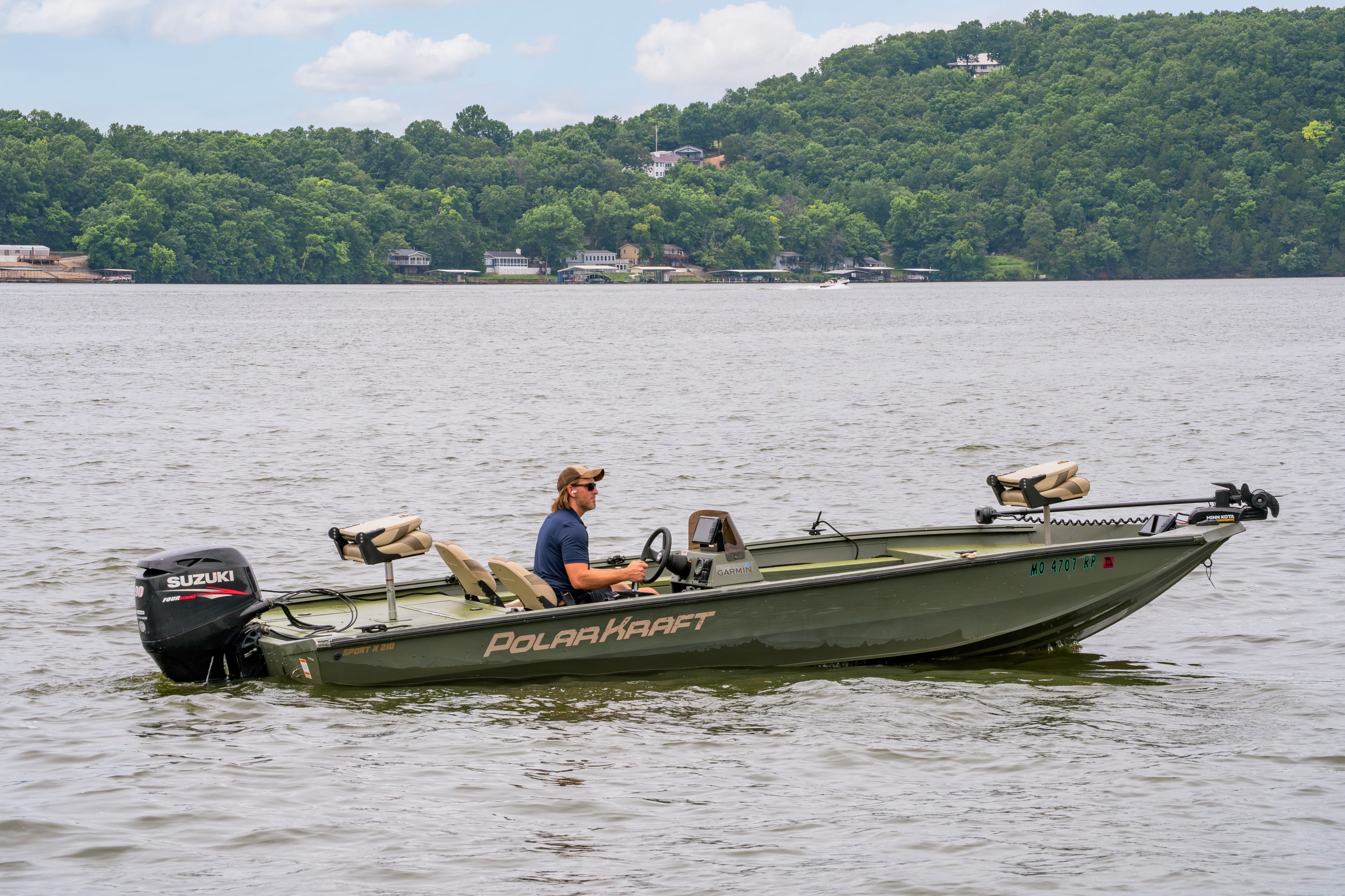 A man fishing in a Polar Kraft boat on a calm lake surrounded by greenery.