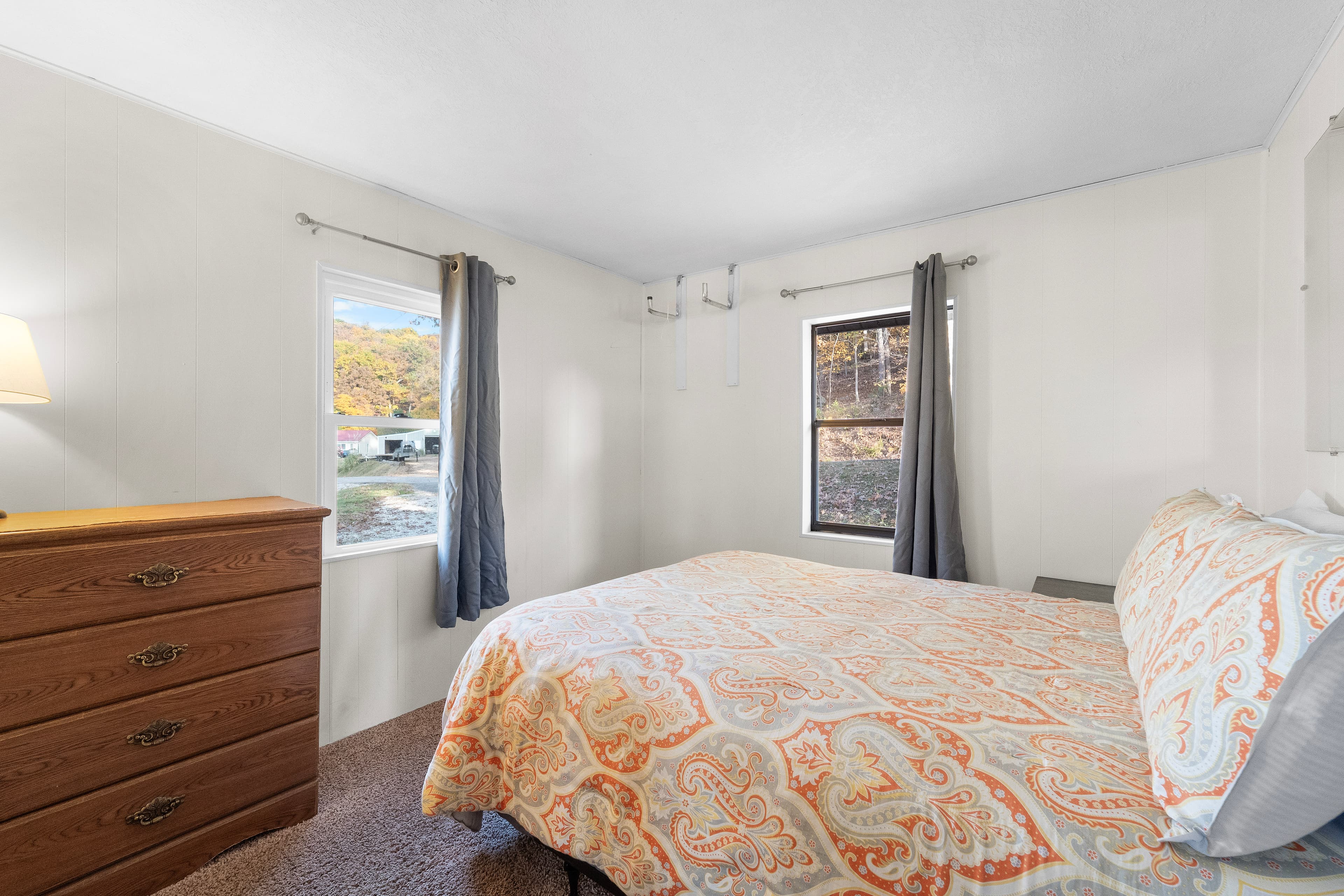 Cozy bedroom featuring a patterned bedspread, wooden dresser, and two windows with curtains.