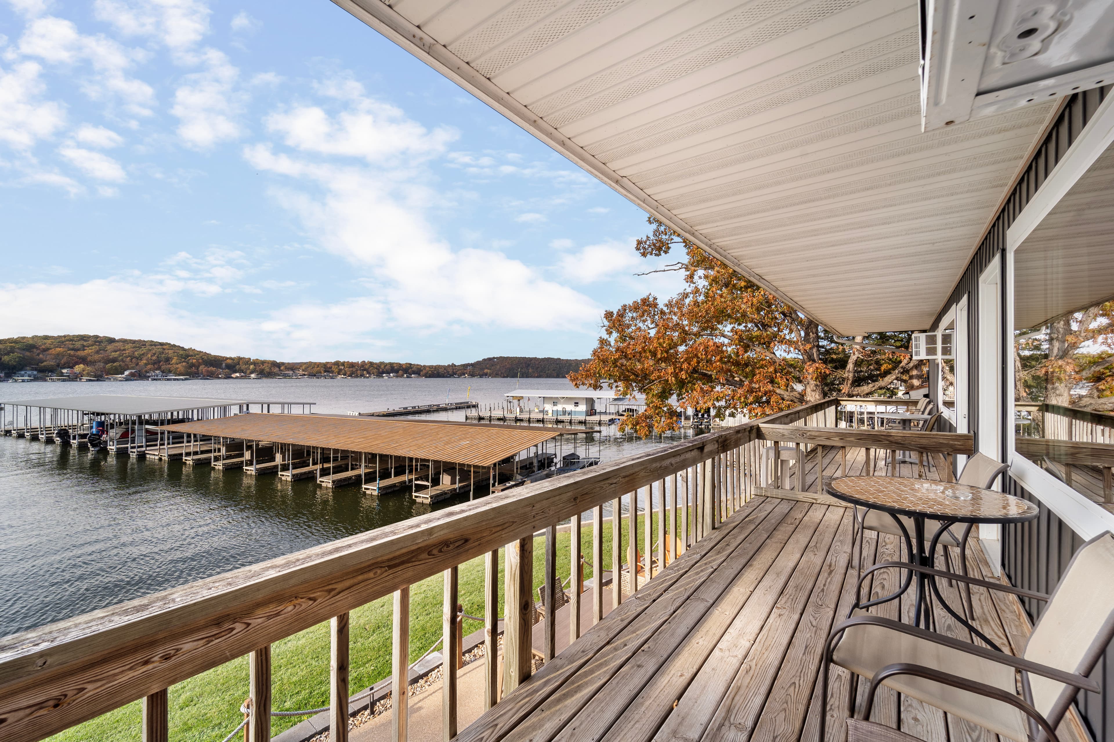 A wooden balcony overlooking a calm lake with boat docks and autumn foliage.