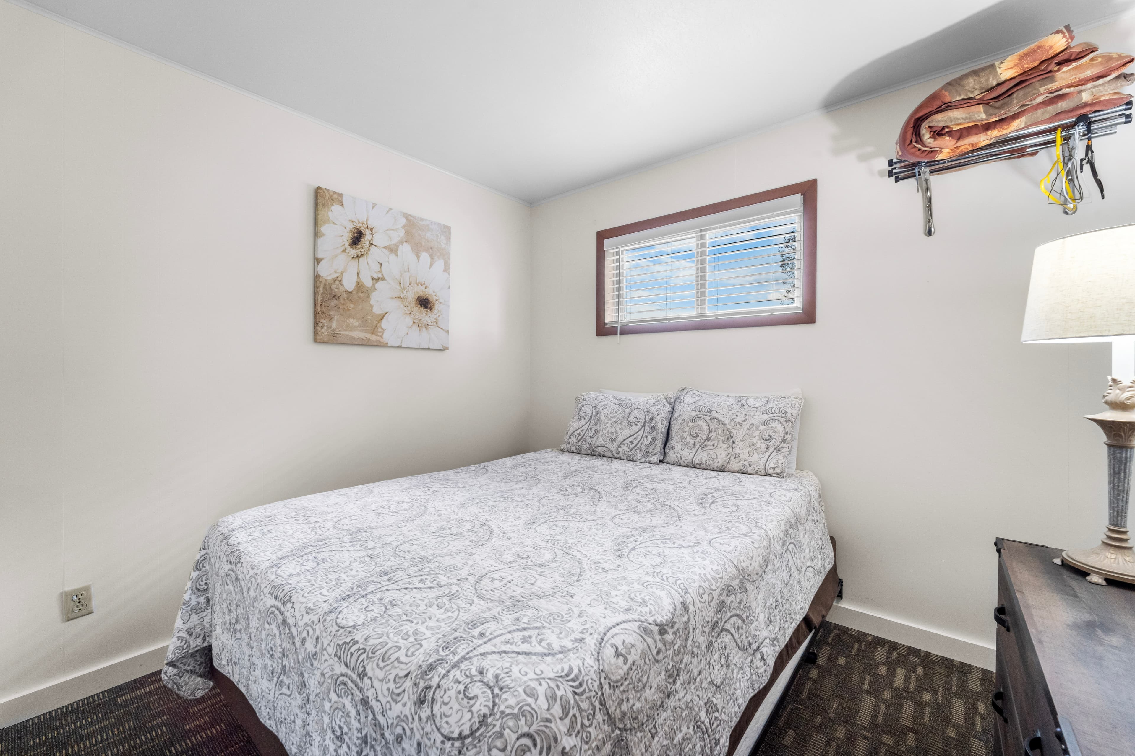 A cozy bedroom featuring a queen-sized bed with a patterned blanket, a window, and decorative wall art.
