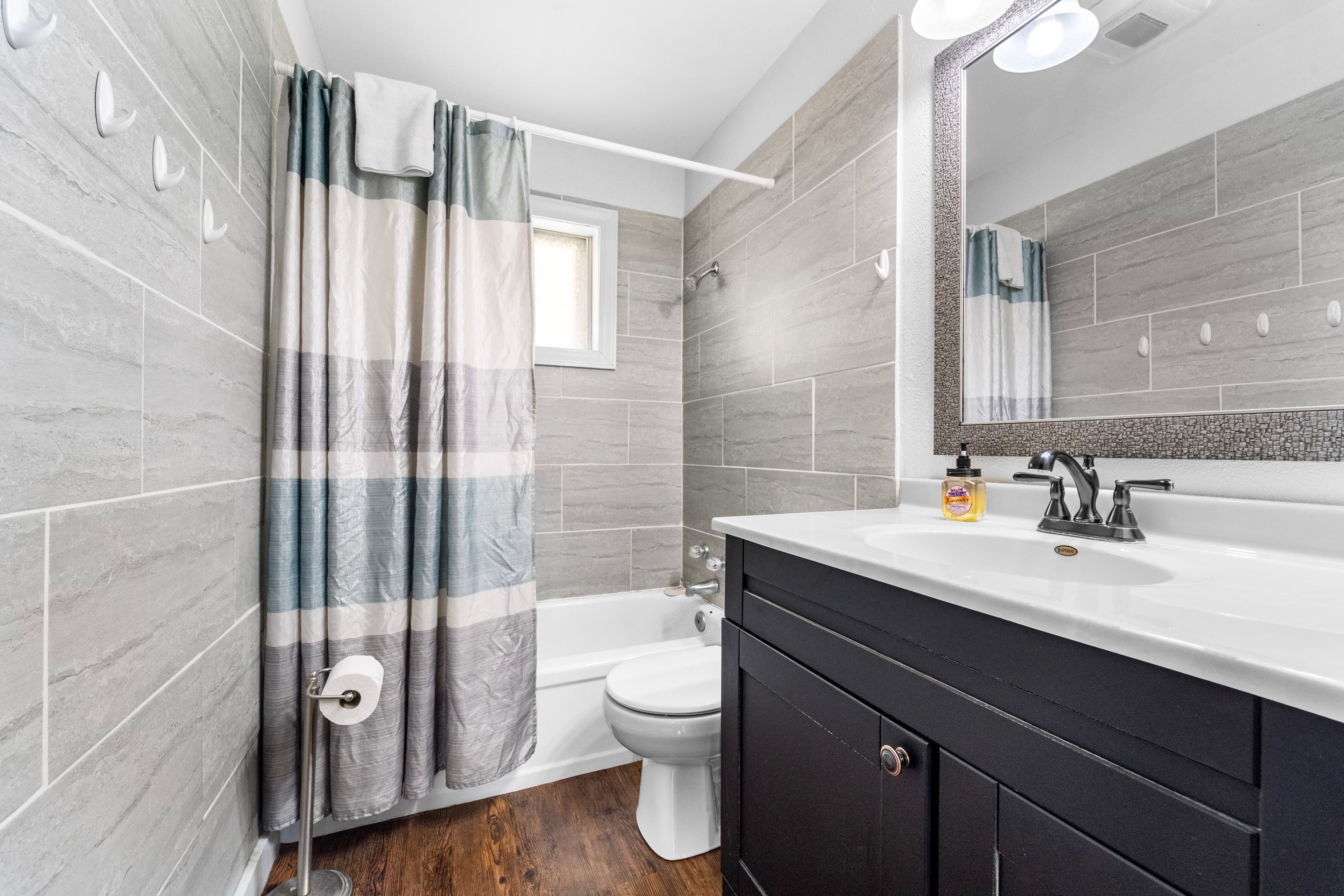 A modern bathroom featuring a shower with a striped curtain, a white sink with a dark cabinet, and gray tiled walls.
