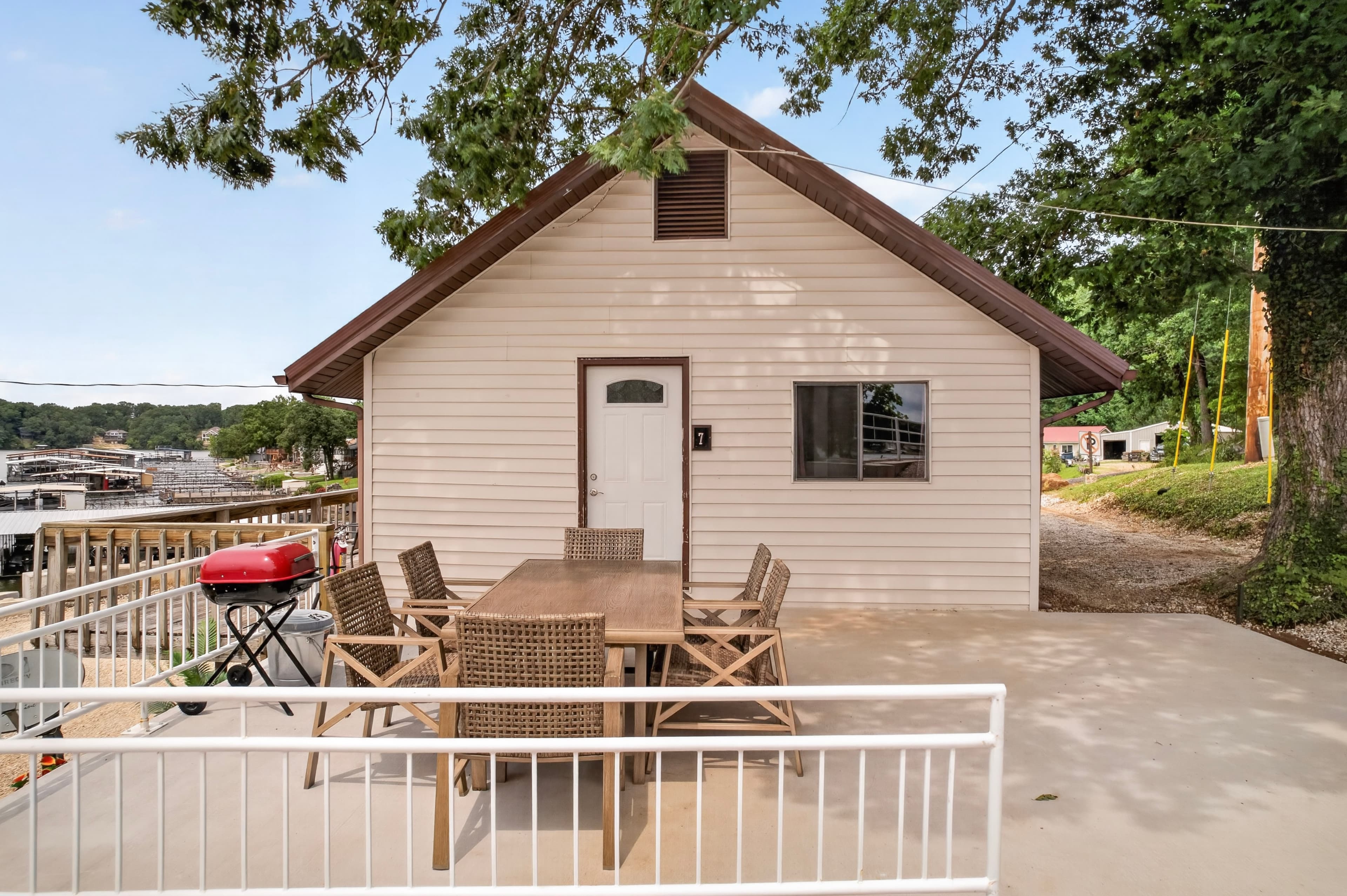 A small beige house with a porch and outdoor dining set, surrounded by trees.