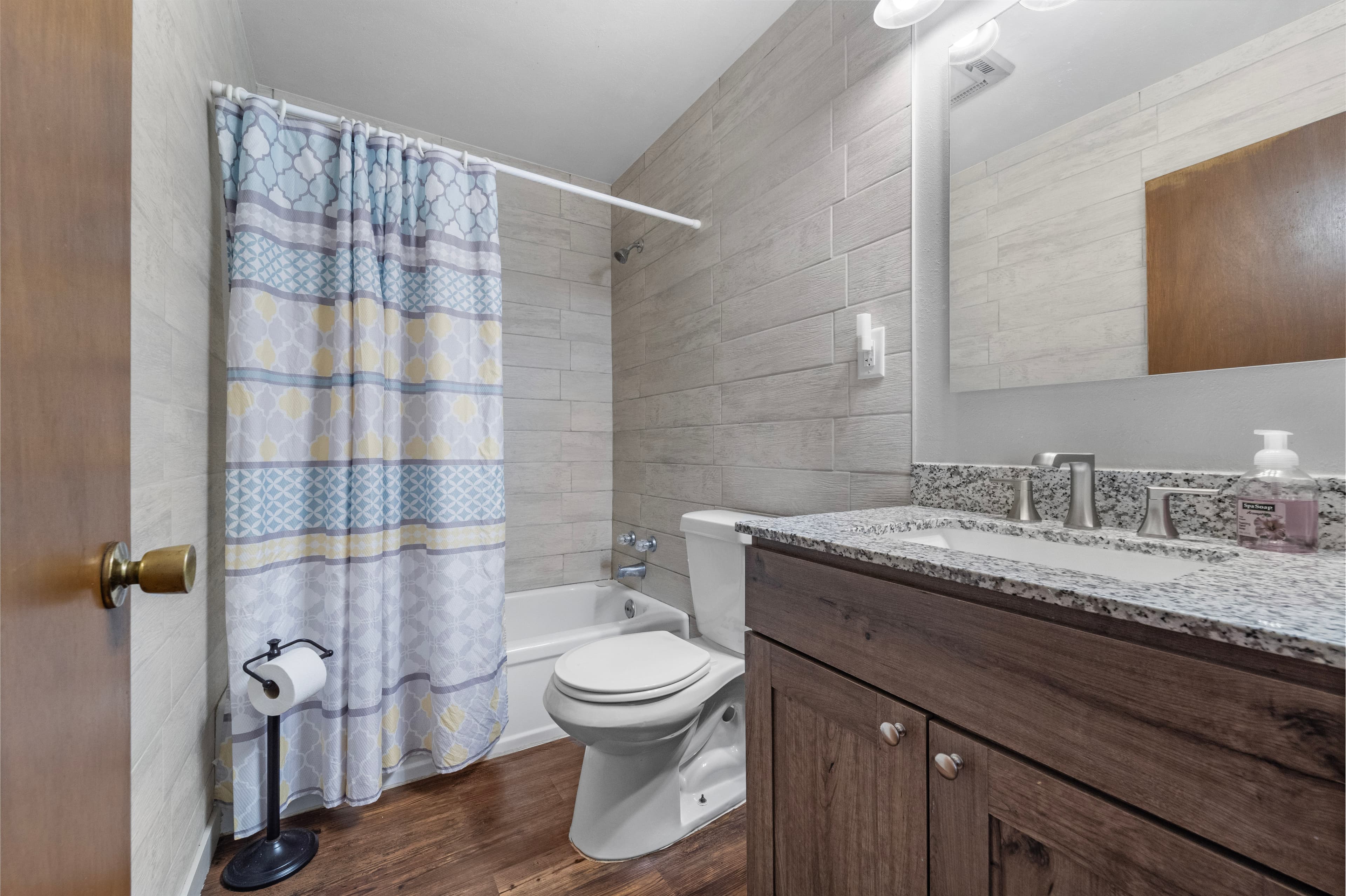 Modern bathroom featuring a bathtub, toilet, and granite vanity with a patterned shower curtain.